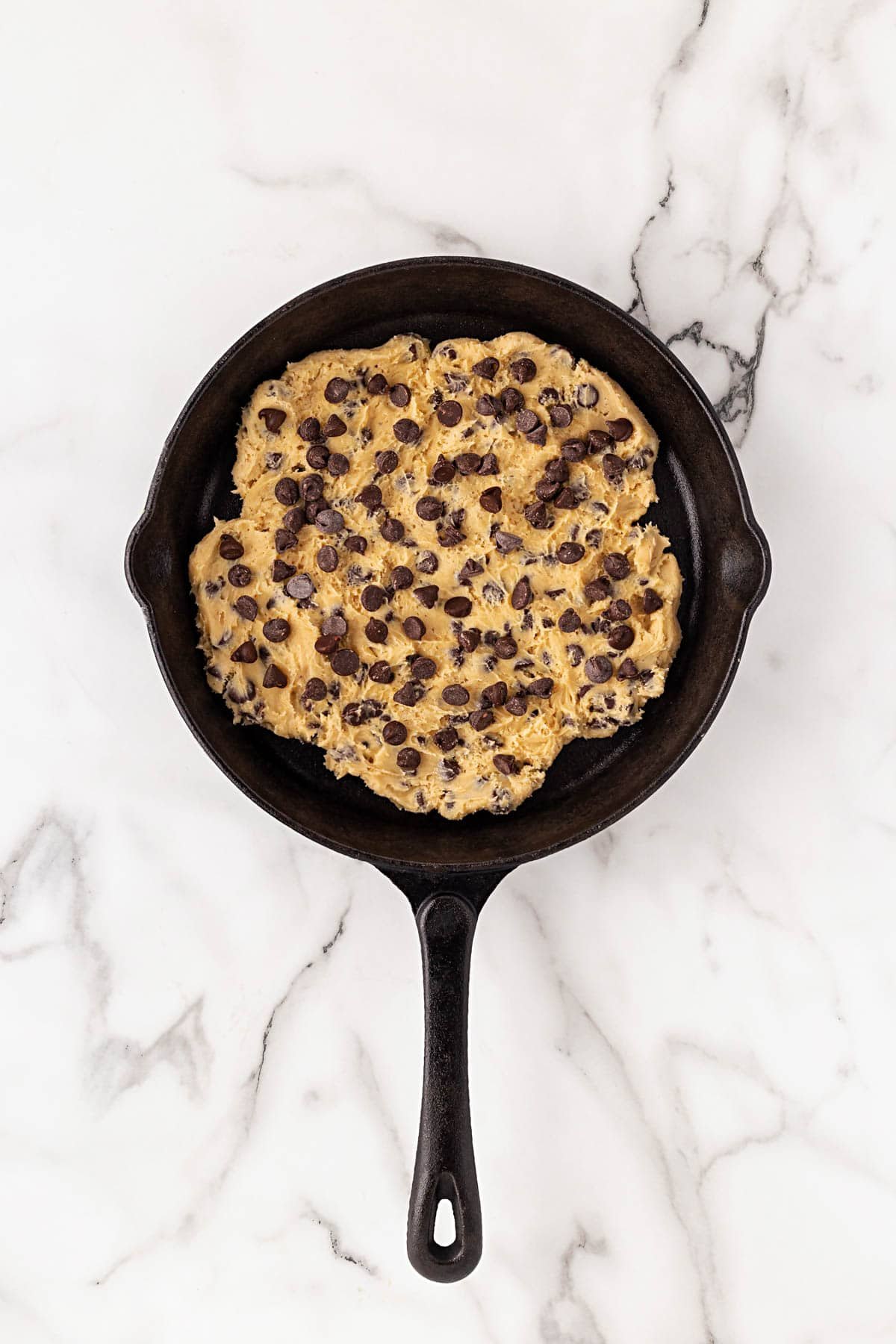 Cookie dough spread evenly in a cast iron skillet and topped with extra chocolate chips before baking