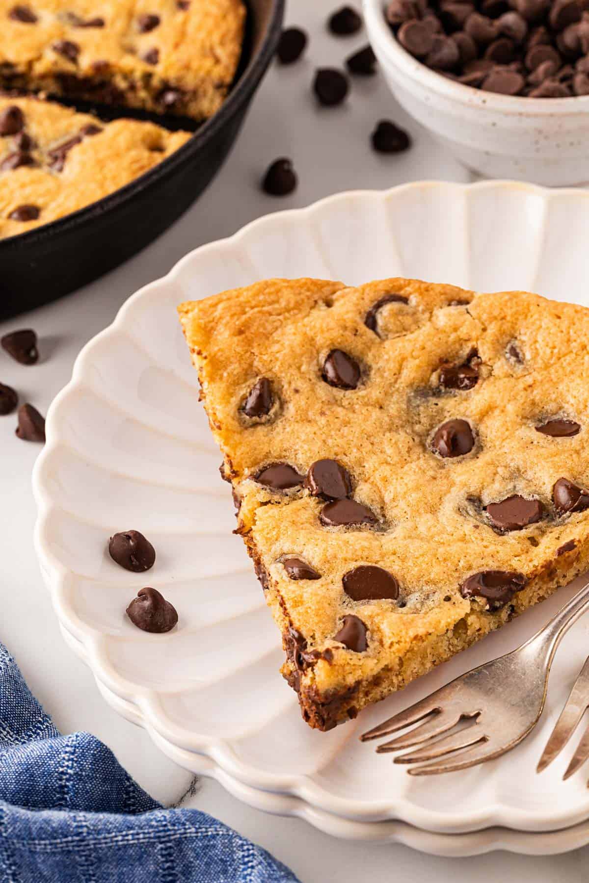 A single slice of chocolate chip skillet cookie served on a white scalloped plate with a fork