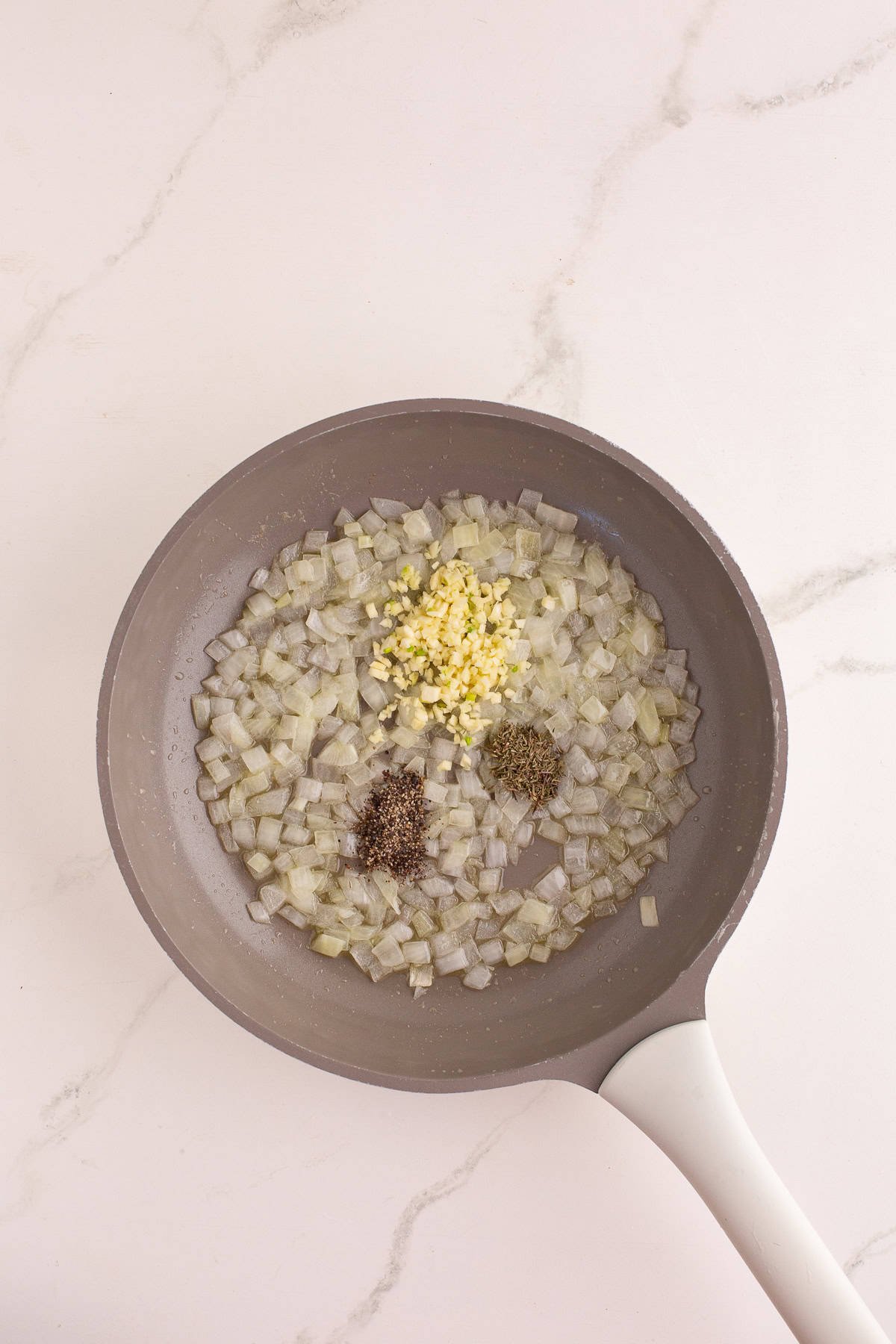 Skillet with diced onions, minced garlic, and dried herbs sautéing together