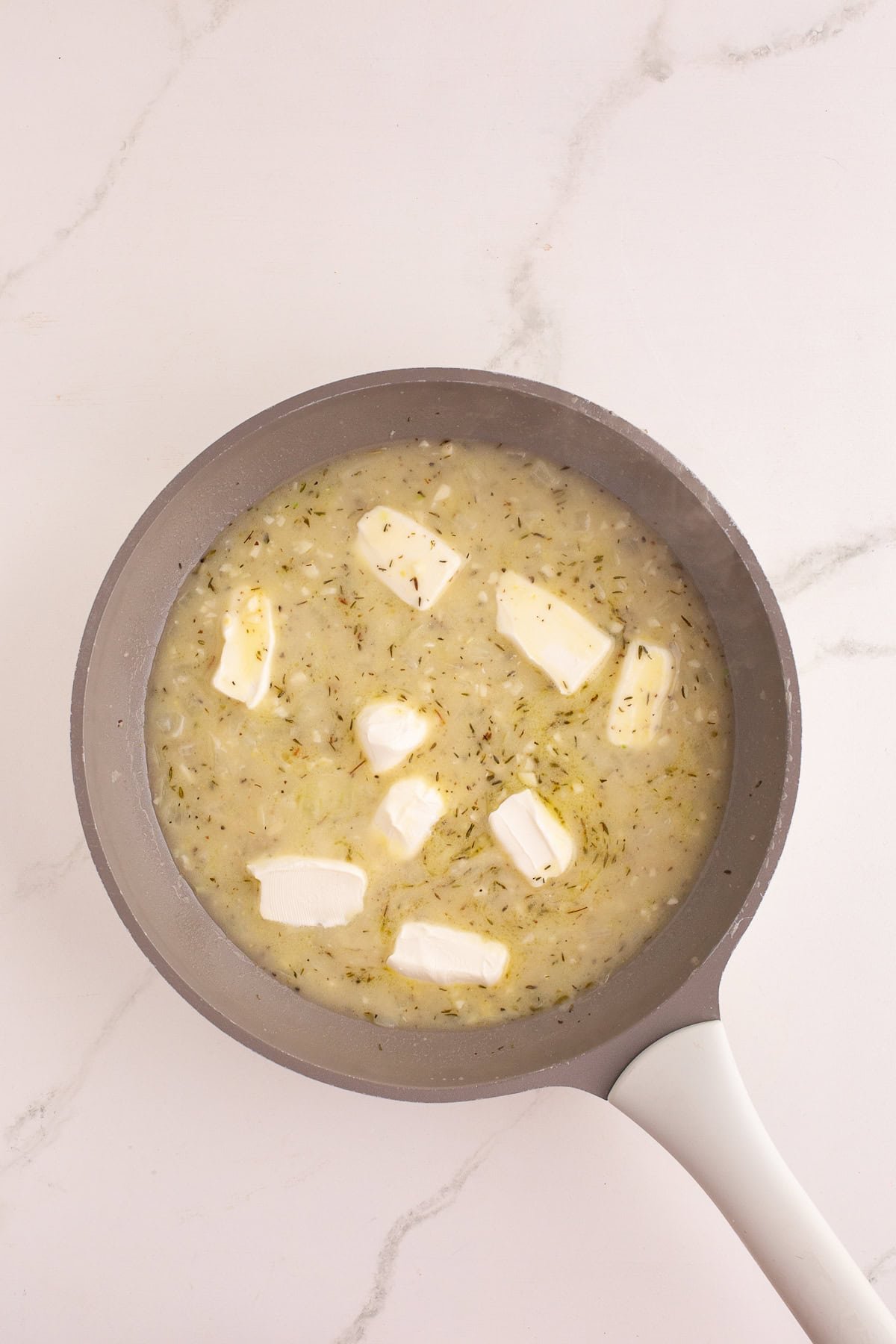 Cubes of cream cheese melting into the creamy onion mixture in the skillet