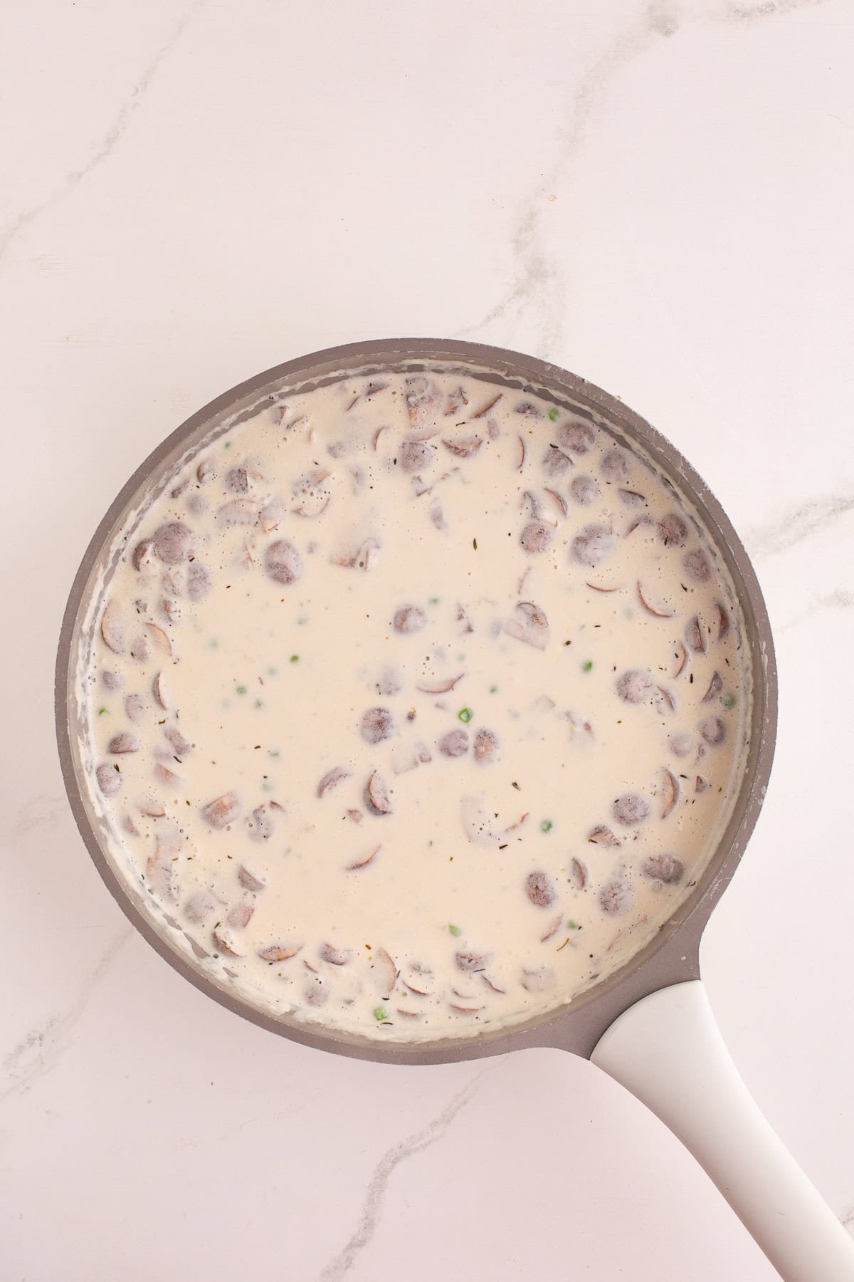 Creamy sauce simmering in the skillet with sliced mushrooms and peas