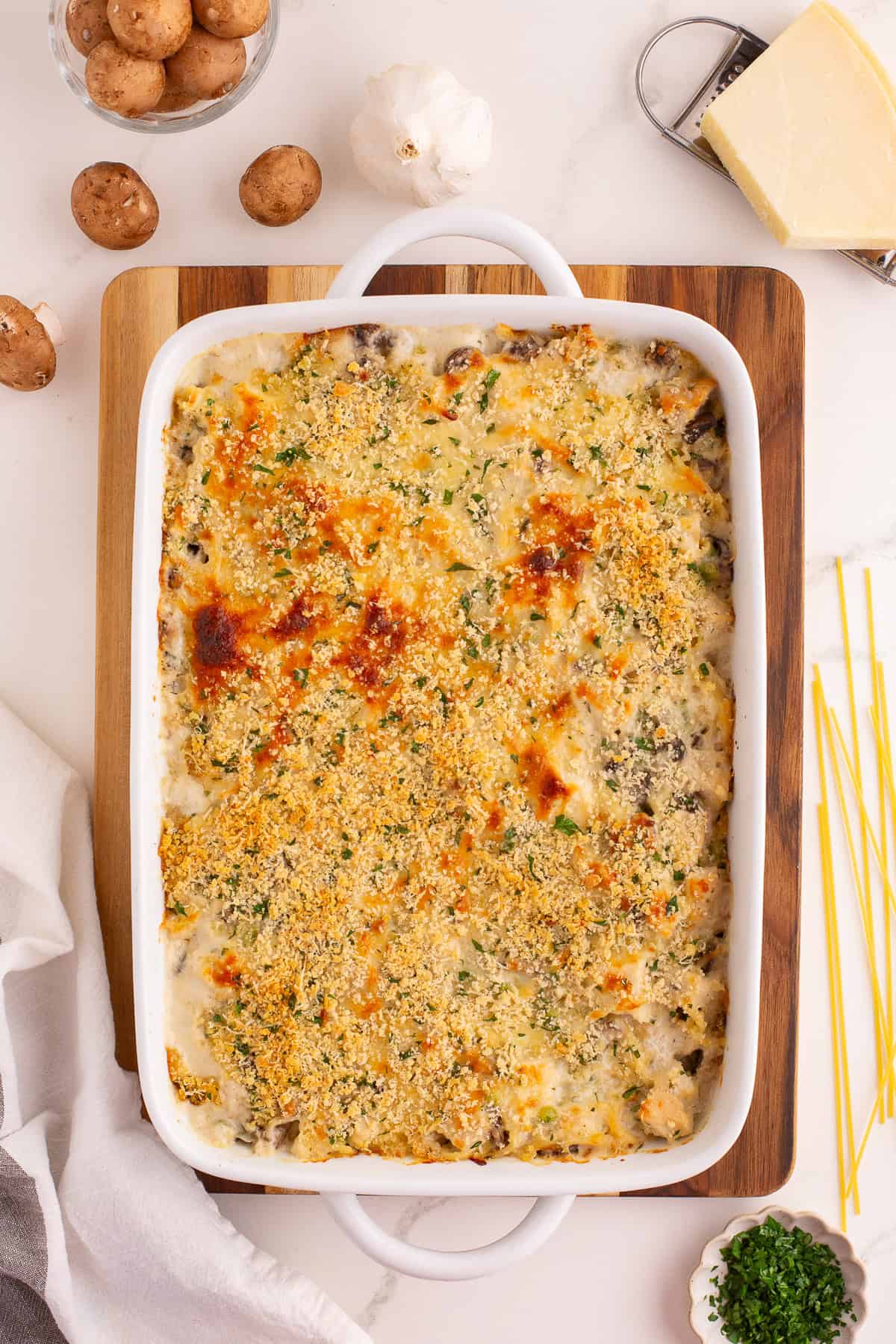 Baked turkey tetrazzini with a golden-brown, cheesy breadcrumb crust, surrounded by mushrooms, garlic, and cheese on the counter