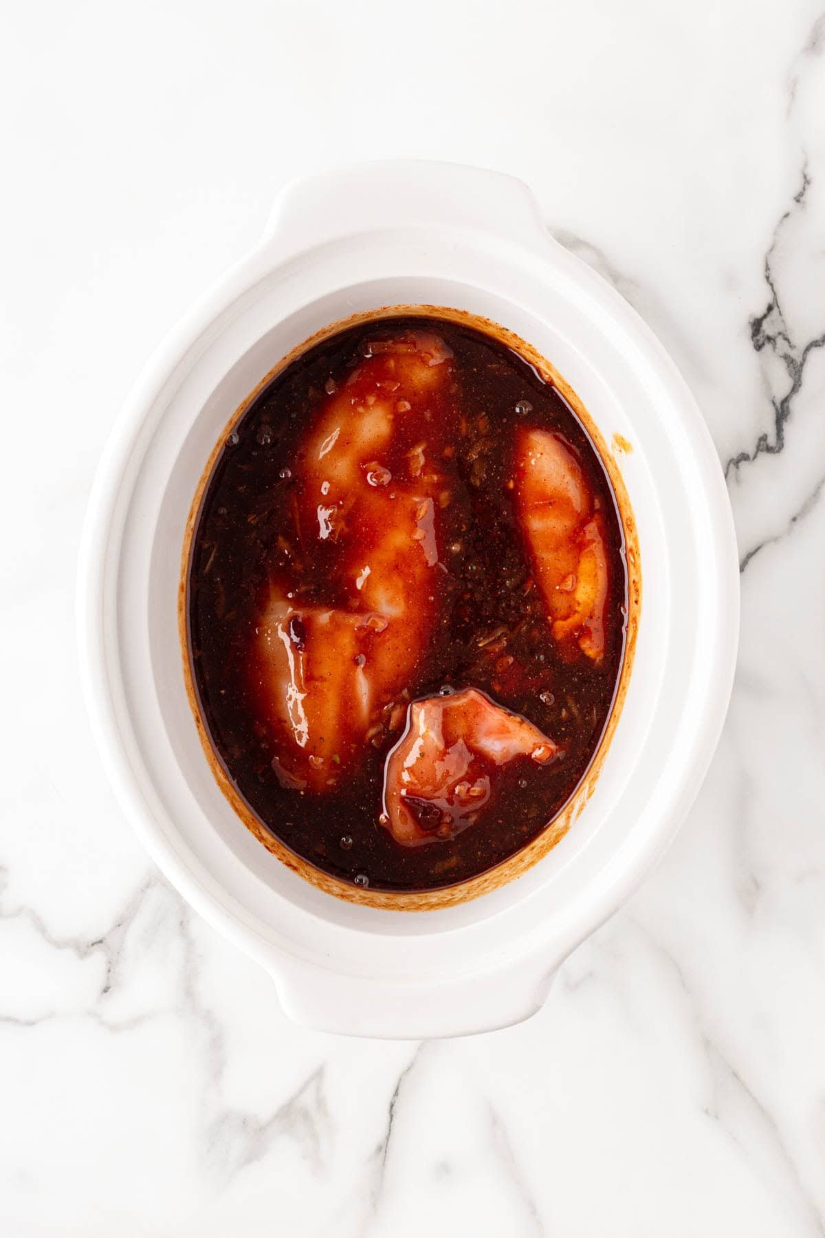 Raw chicken breasts covered in barbecue sauce mixture inside a slow cooker