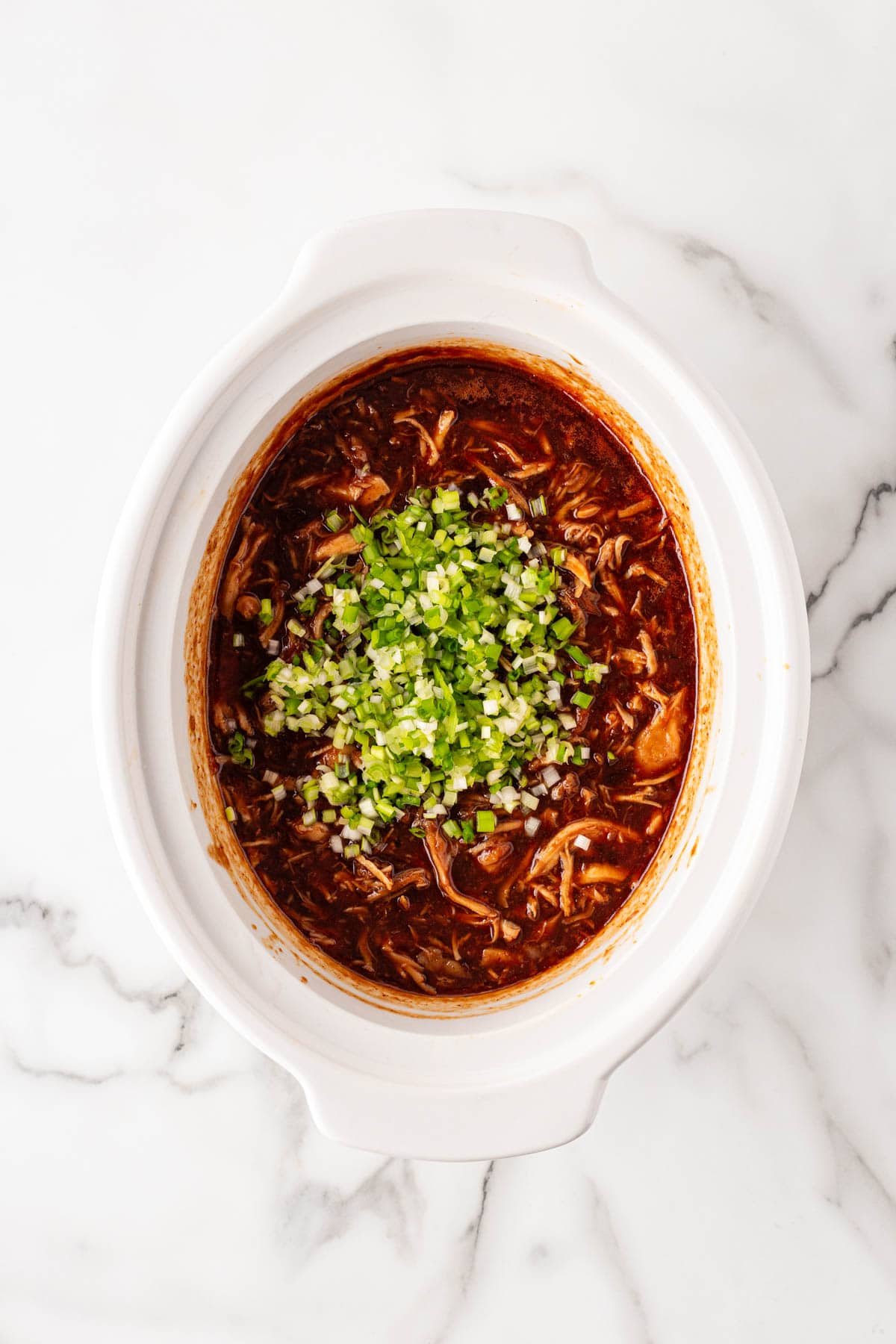 Finished barbeque shredded slow cooker chicken in the crockpot, topped with minced green onions