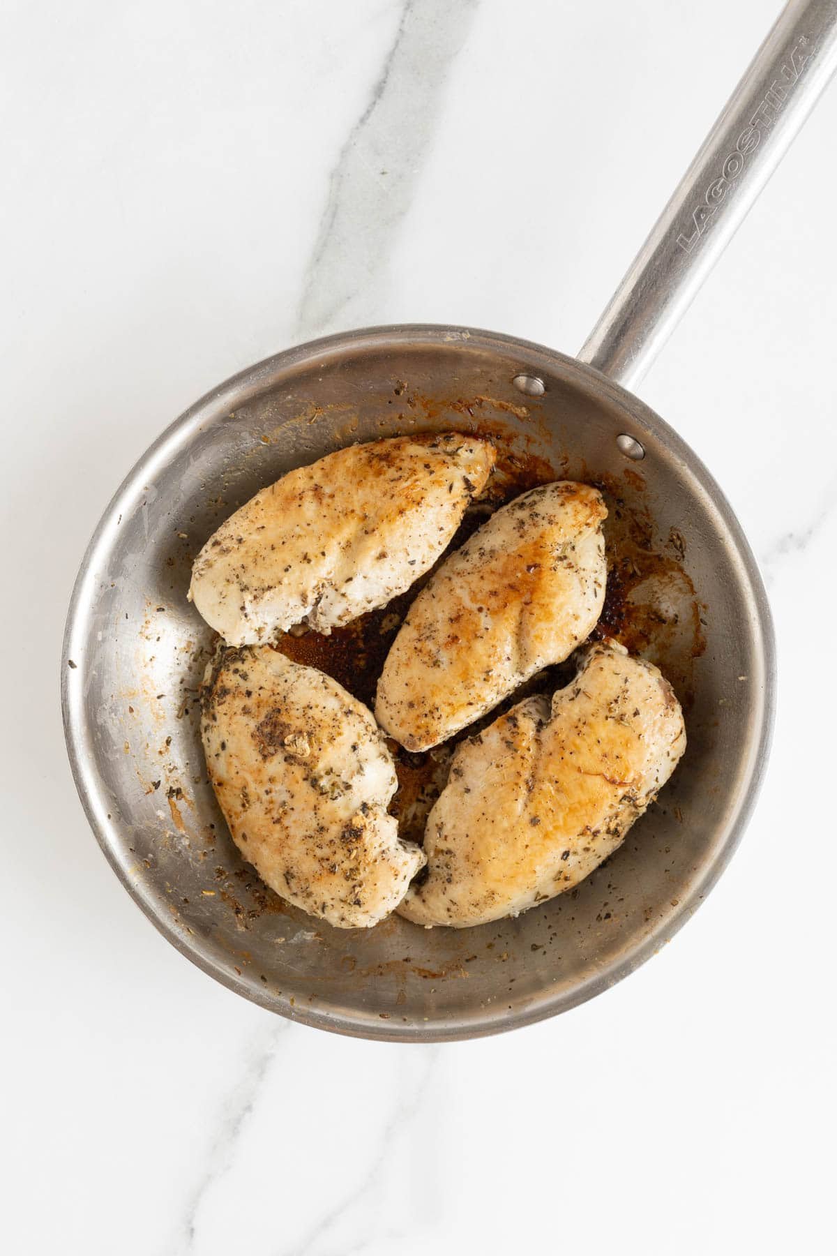 Seasoned chicken breasts seared in a stainless steel skillet until lightly golden