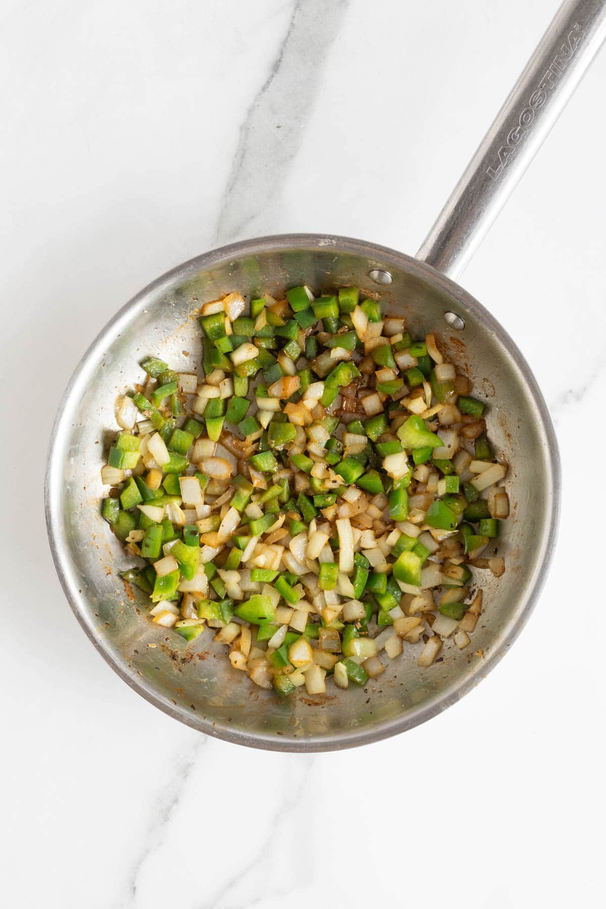 Chopped green bell peppers and onions sautéing in a skillet until softened