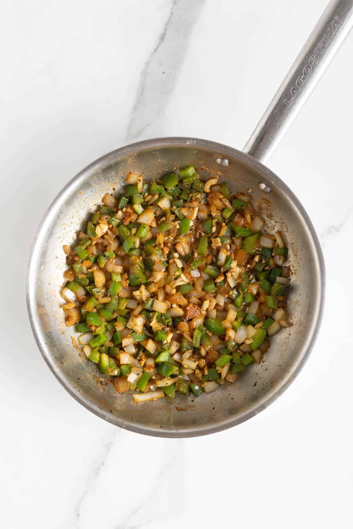 Bell peppers, onions, and garlic cooking with spices in a skillet, lightly browned and fragrant