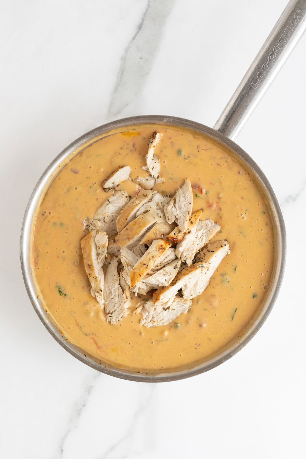 Sliced cooked chicken breasts added to a creamy sauce in a skillet