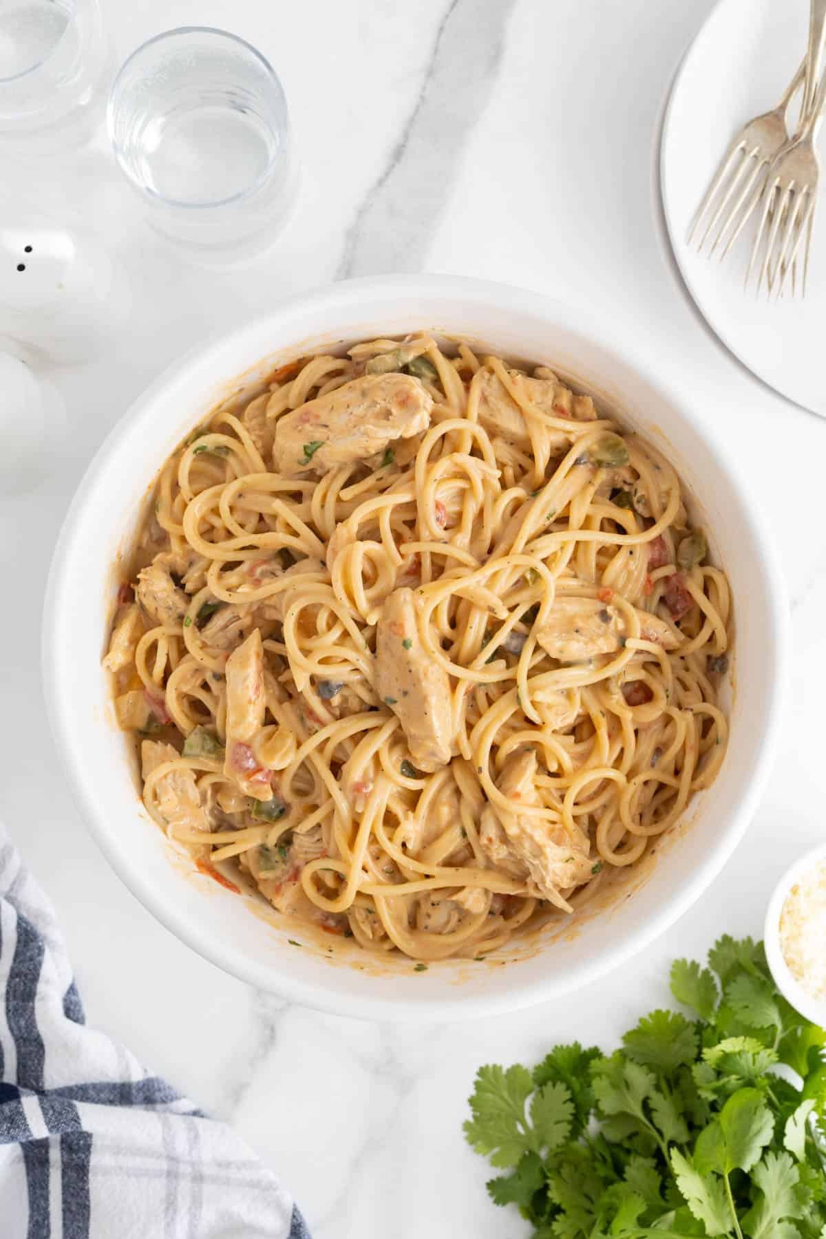Overhead shot of creamy chicken spaghetti tossed in sauce and served in a white bowl on a marble surface