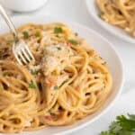 Fork twirling cheesy chicken spaghetti topped with grated cheese and fresh herbs on a plate