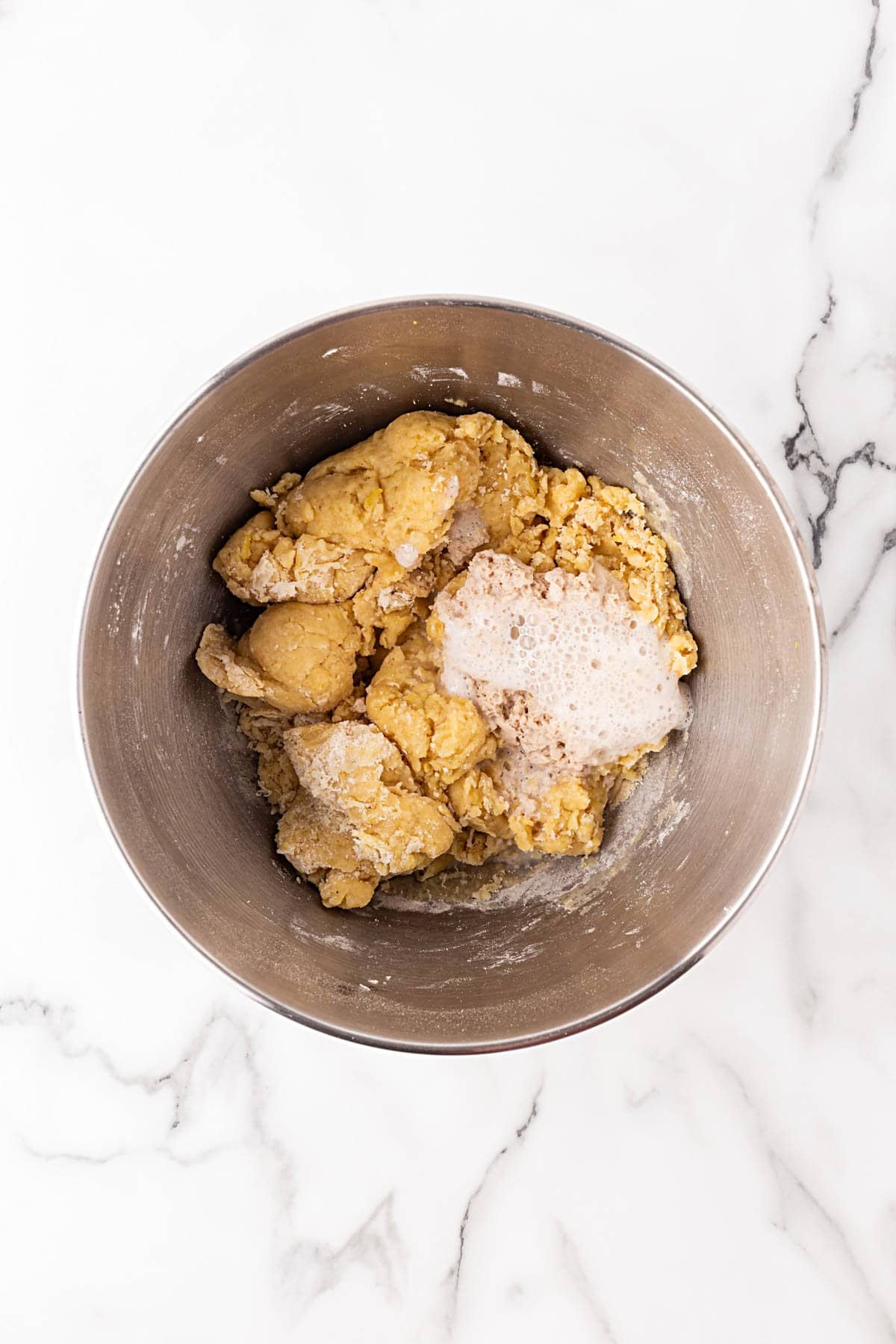 Shaggy king cake dough in a stand mixer bowl with foamy yeast added on top