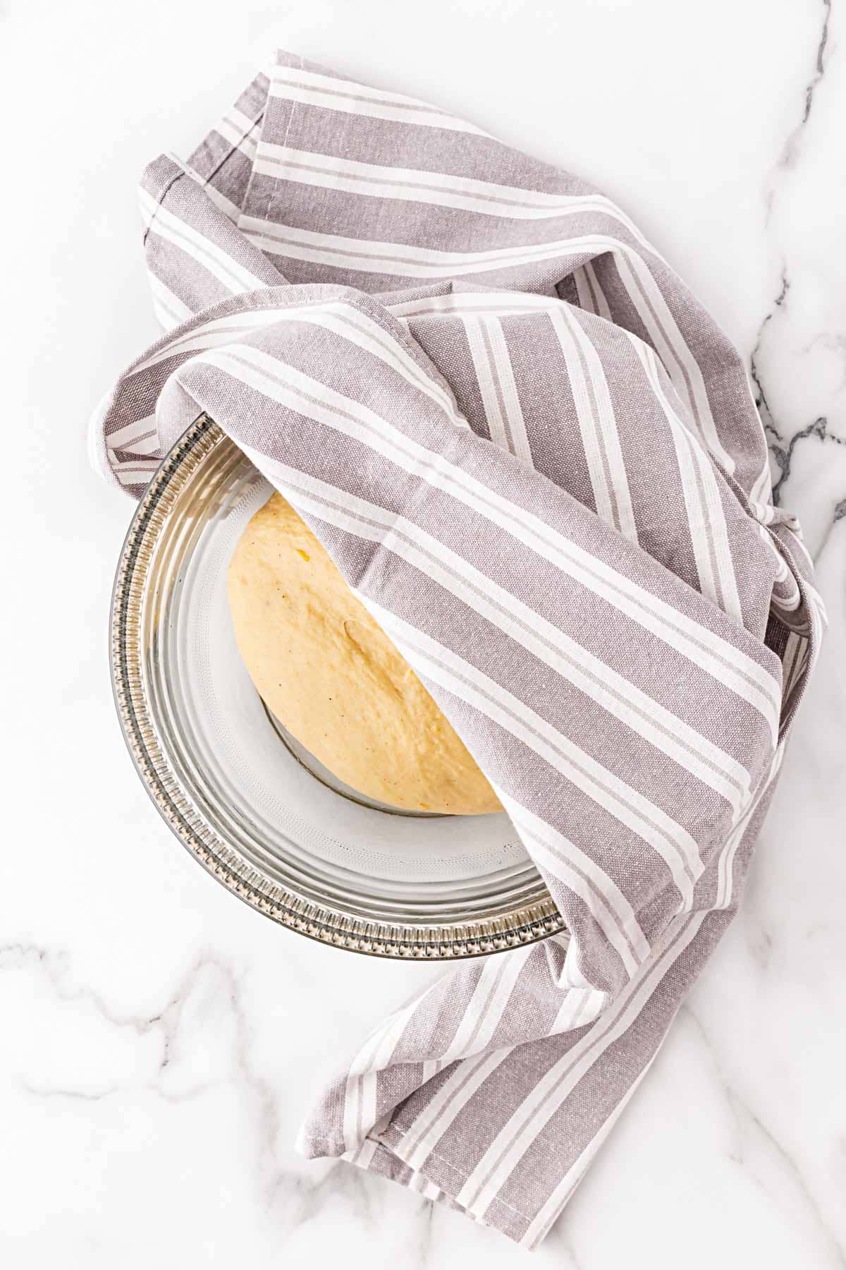 Dough resting in a greased bowl, covered with a striped kitchen towel