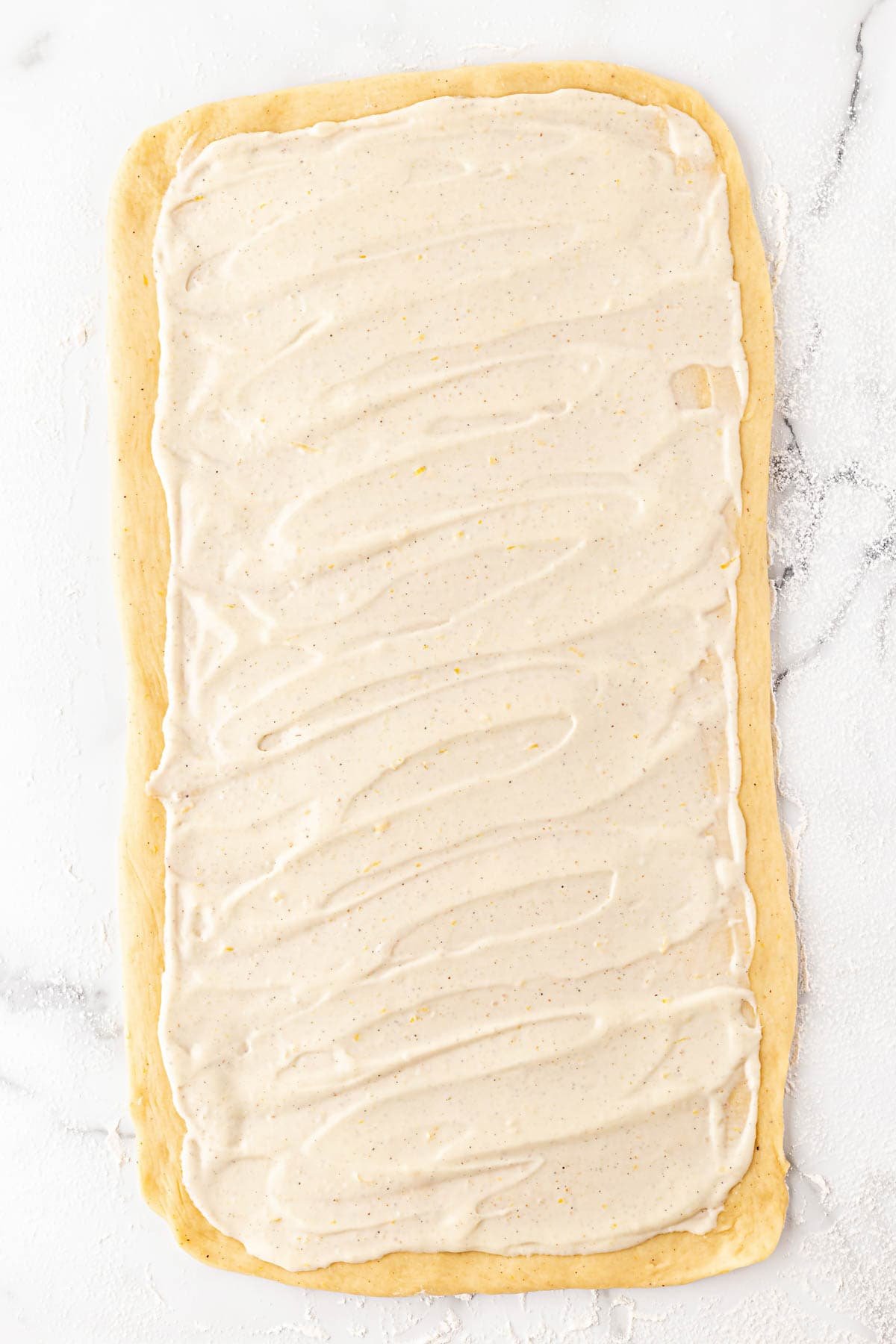 Rolled dough rectangle spread evenly with creamy filling on a floured surface