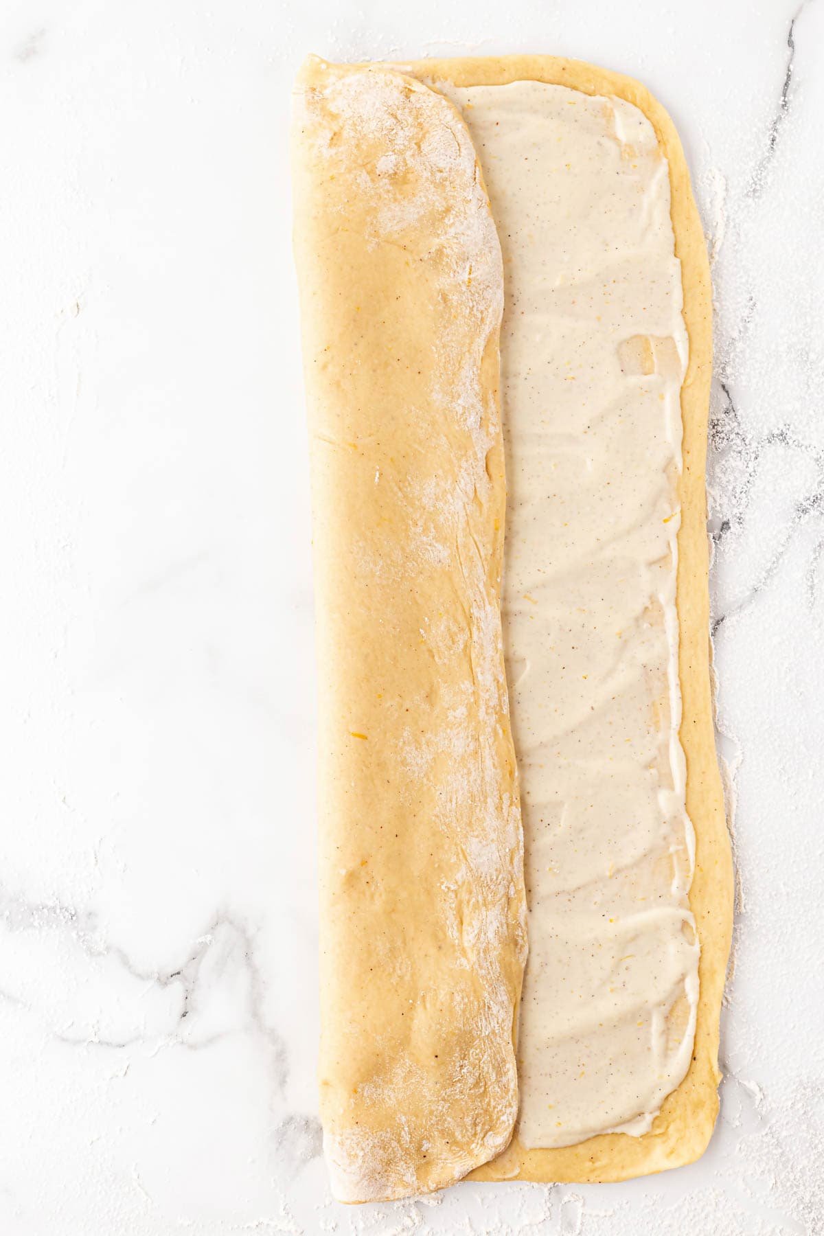 Dough rectangle being rolled into a long log over the filling