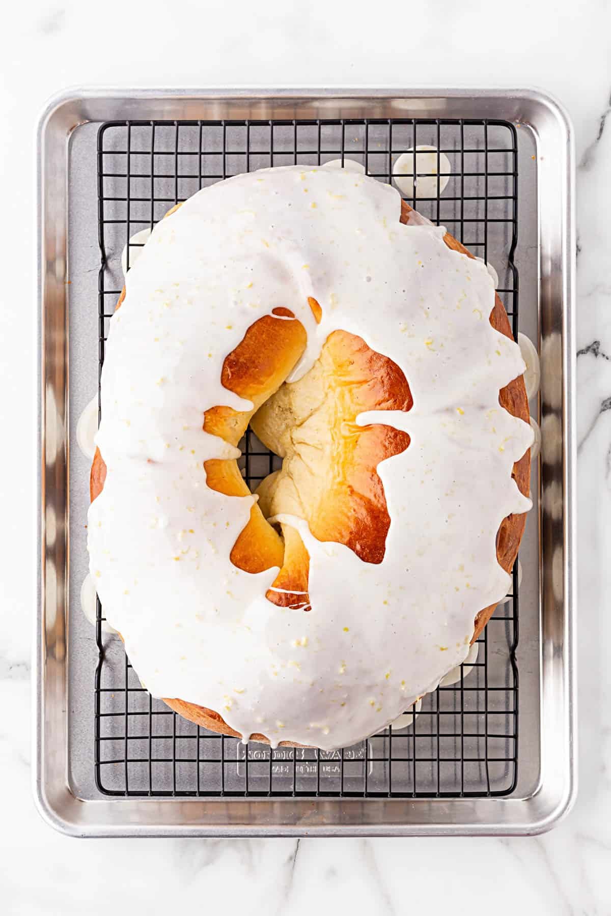 King cake covered in white icing cooling on a wire rack over a baking sheet