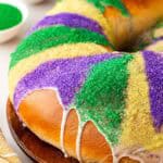 Closeup of a king cake topped with purple, green, and gold sanding sugar and white icing