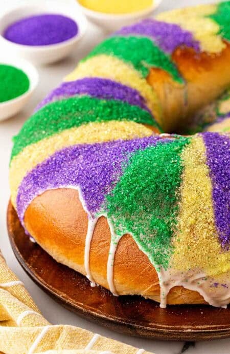 Closeup of a king cake topped with purple, green, and gold sanding sugar and white icing