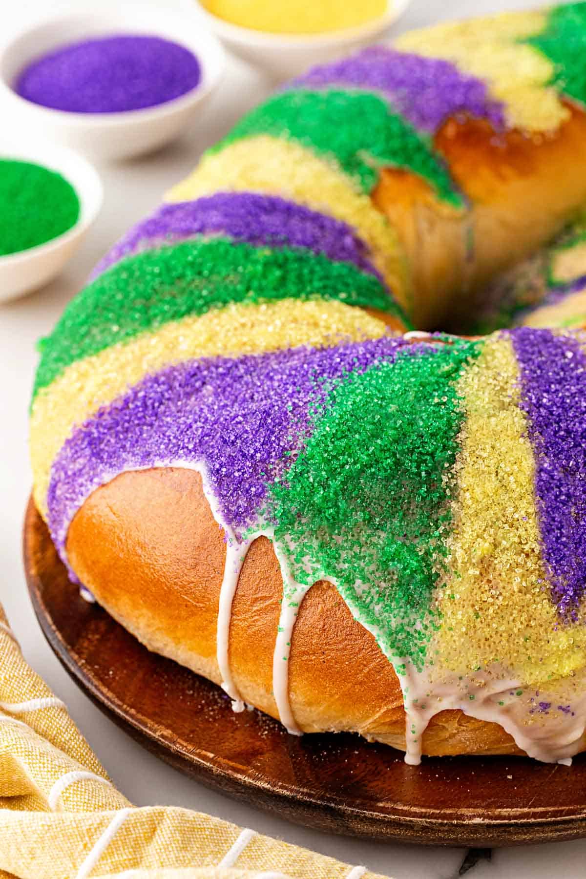 Closeup of a king cake topped with purple, green, and gold sanding sugar and white icing