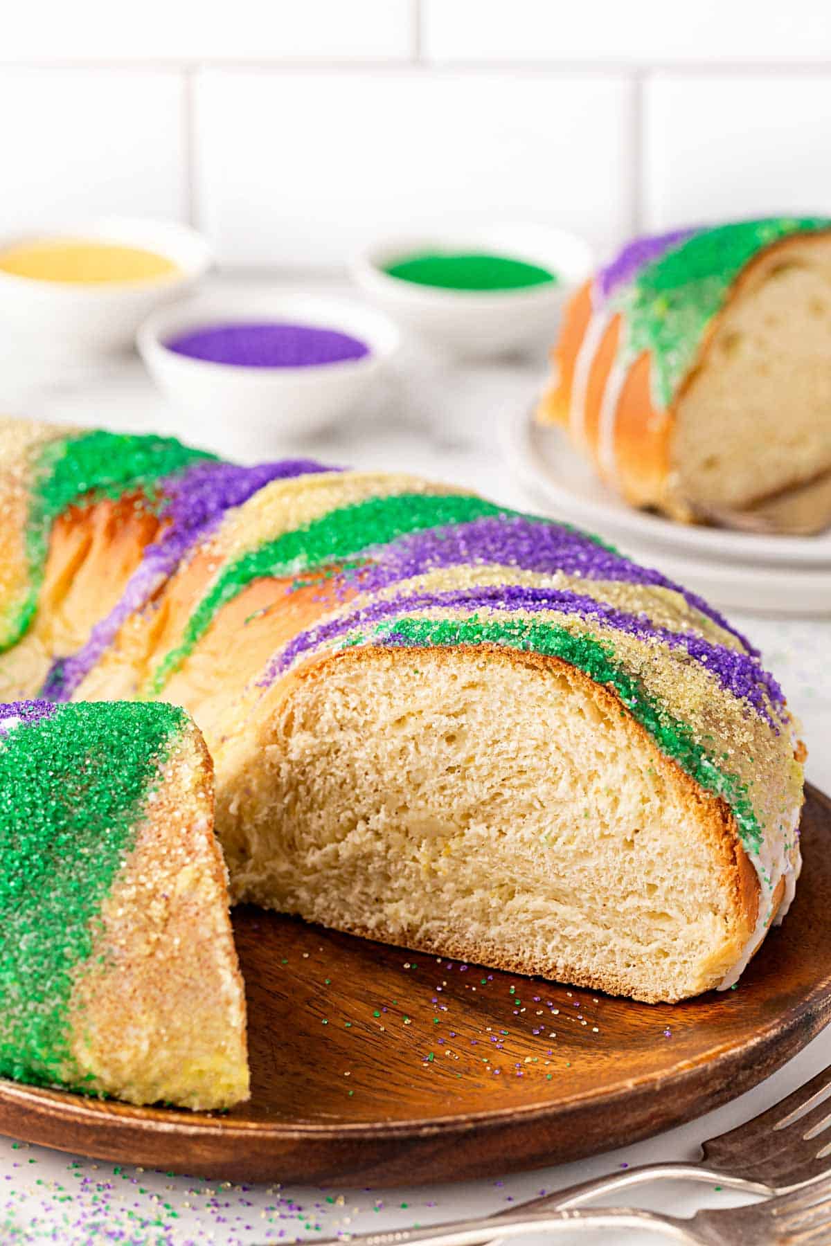 Slice of king cake showing soft, fluffy interior with colorful sugar topping on a wooden plate