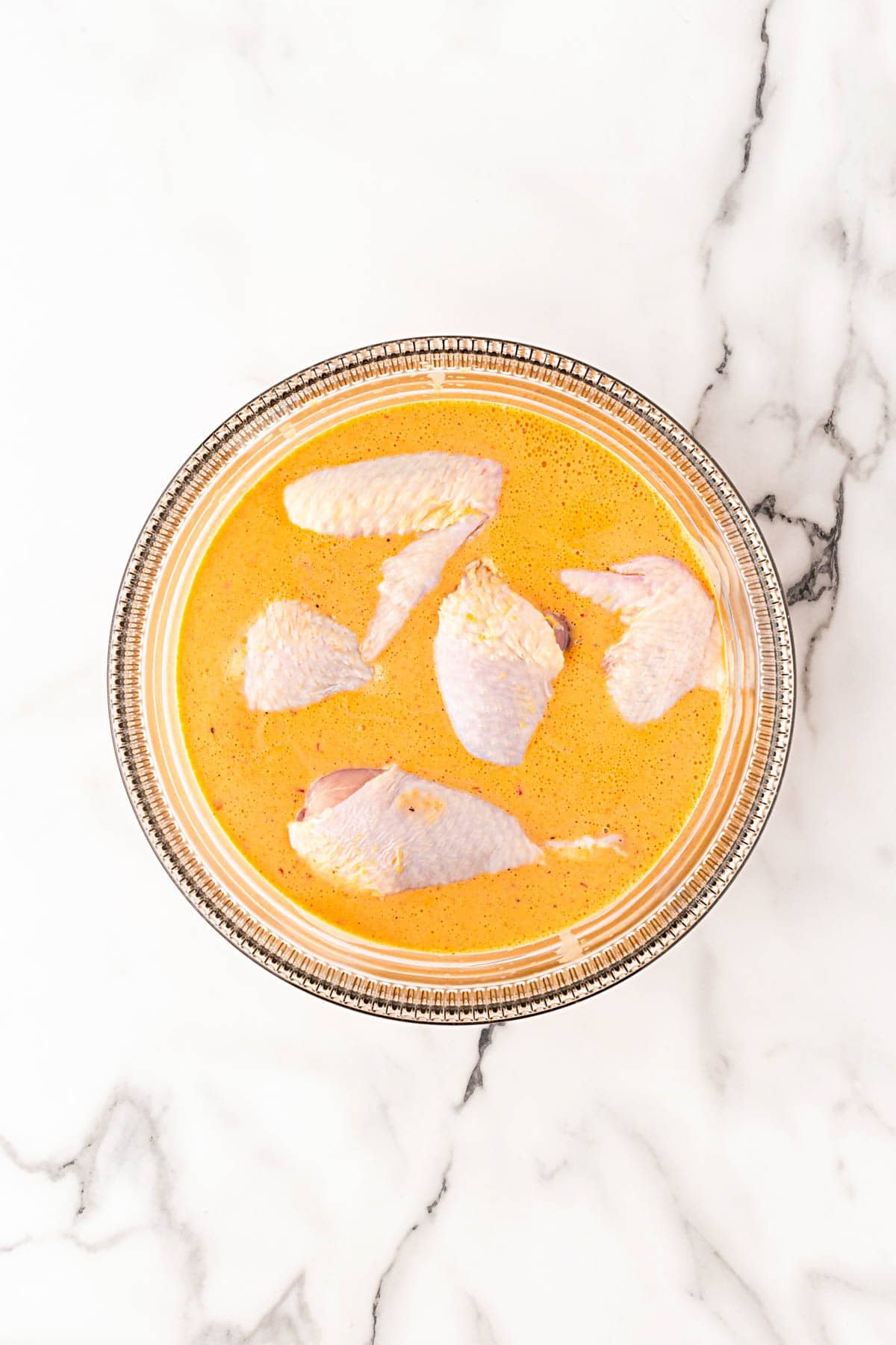 Raw chicken pieces soaking in orange-colored spicy buttermilk marinade
