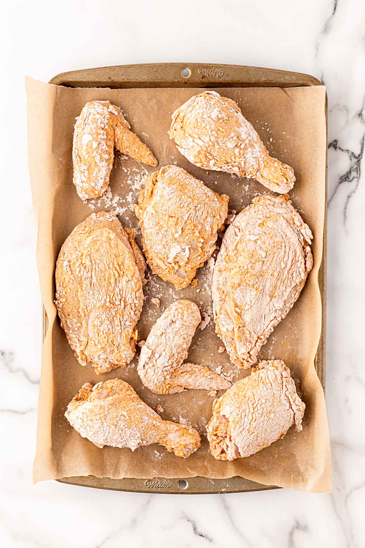 Flour-coated chicken pieces arranged on a parchment-lined baking sheet