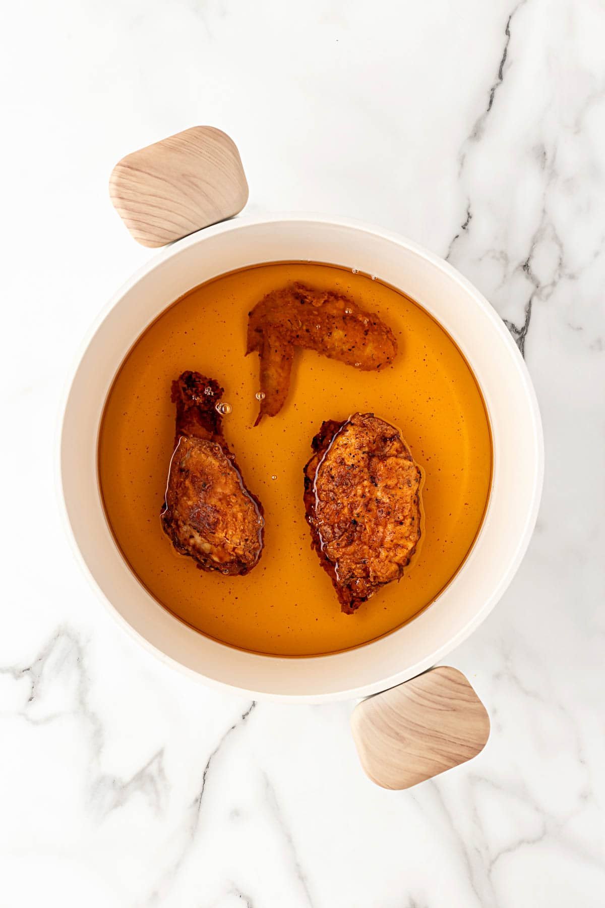 Chicken frying in hot oil inside a white Dutch oven