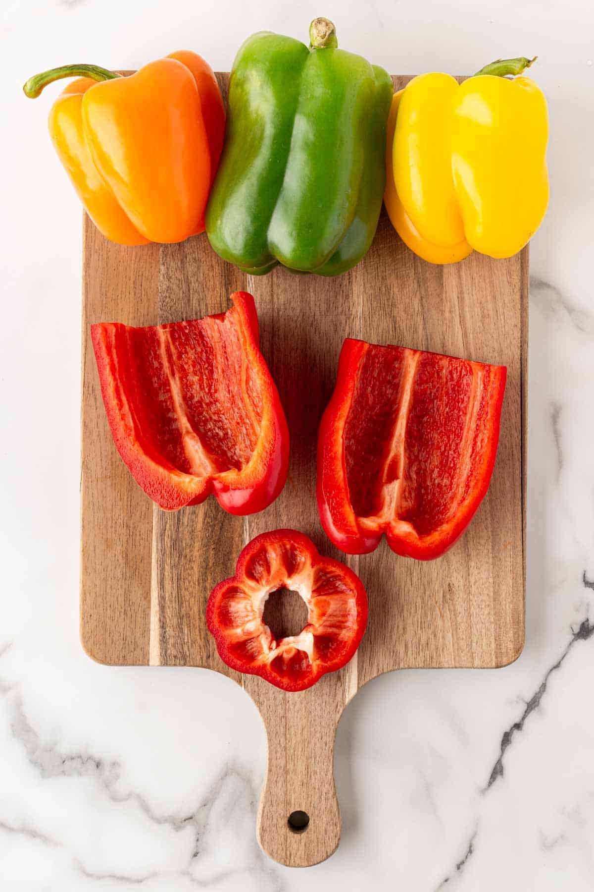 Whole and halved bell peppers arranged on a wooden cutting board