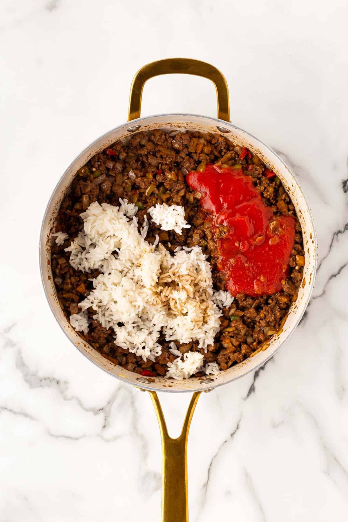 Ground beef mixture in a skillet topped with white rice and tomato sauce before mixing
