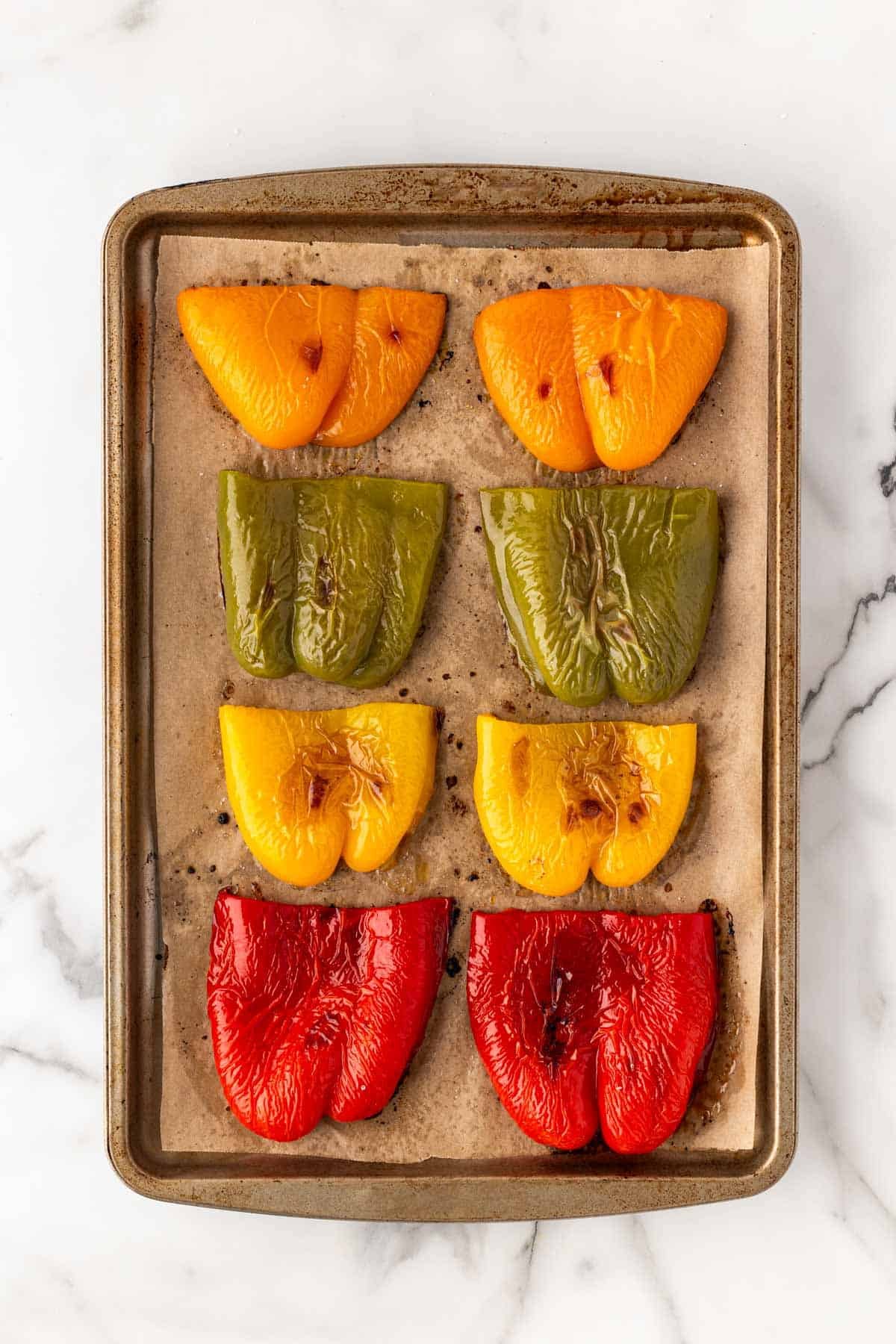 Roasted bell pepper halves arranged on a parchment-lined baking sheet