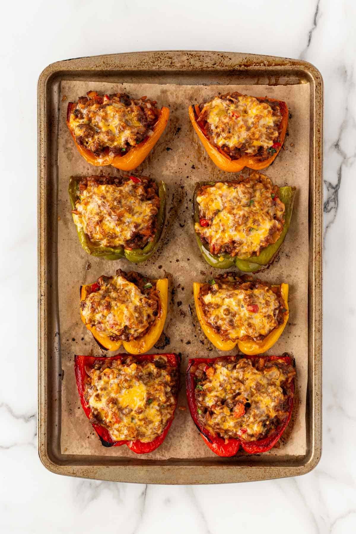 Fully baked stuffed peppers with melted cheese on a baking sheet