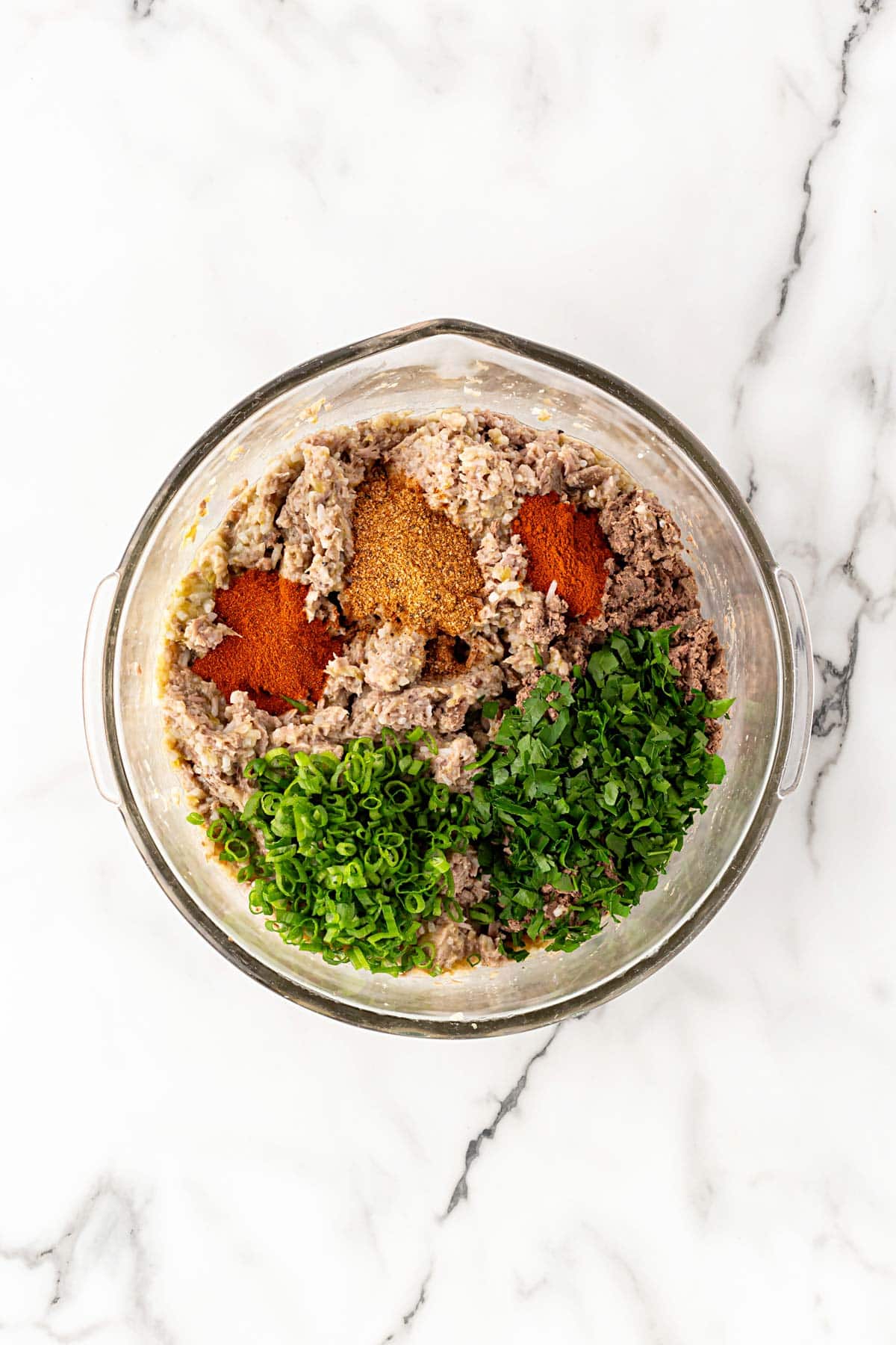 Boudin mixture with spices, chopped parsley, and green onions in a mixing bowl