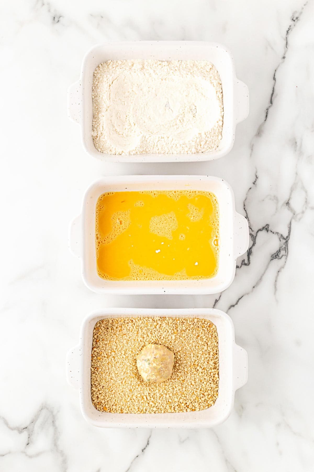 Breading station with flour, beaten eggs, and seasoned breadcrumbs for boudin balls
