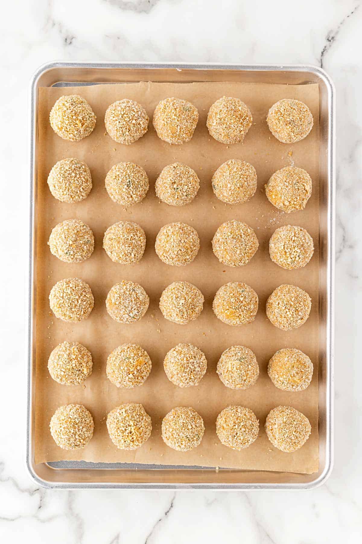 Raw breaded boudin balls arranged on a parchment-lined baking sheet