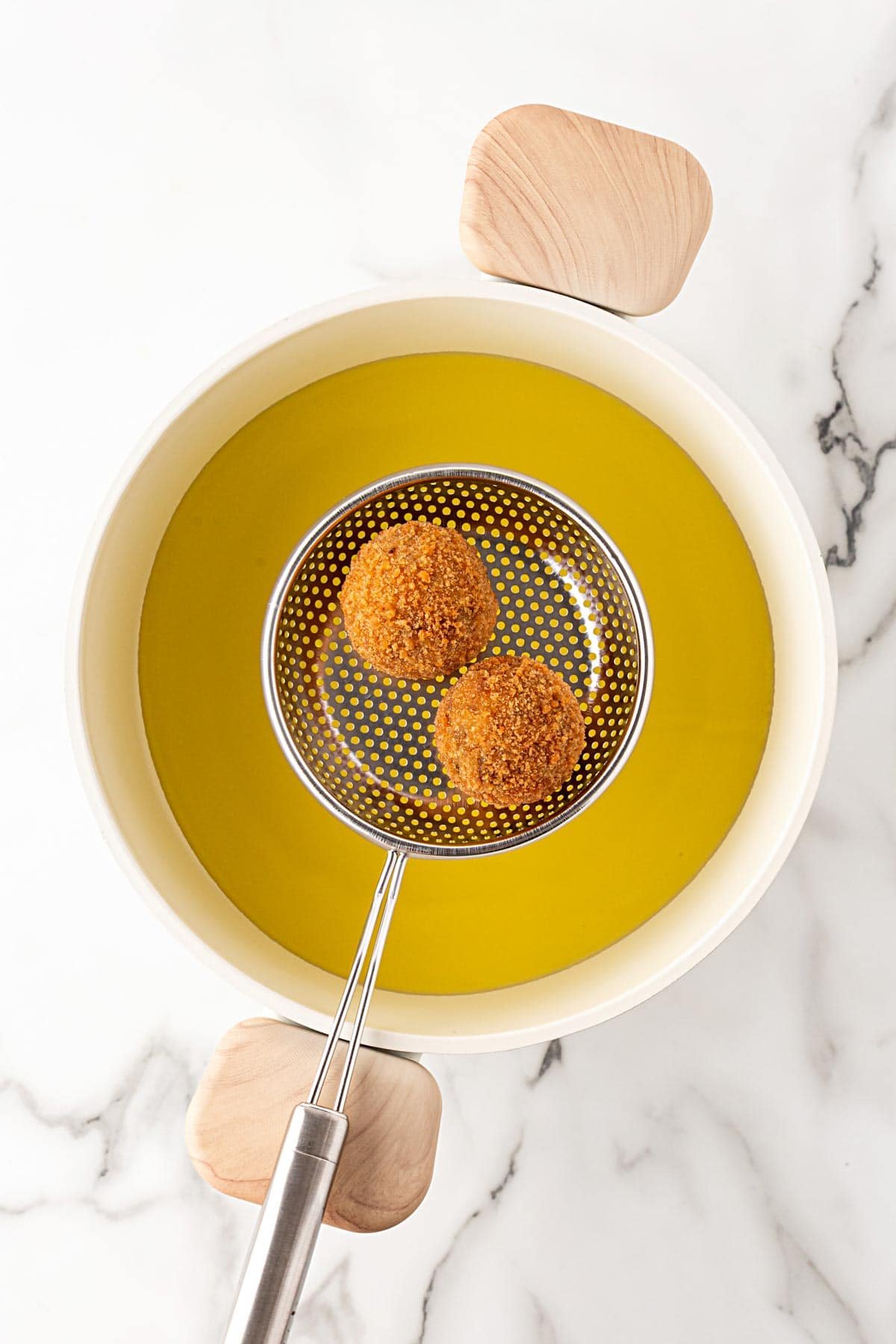 Two boudin balls frying in hot oil, resting in a slotted spoon above the pot