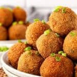 Closeup of crispy fried boudin balls piled in a bowl with green onion garnish