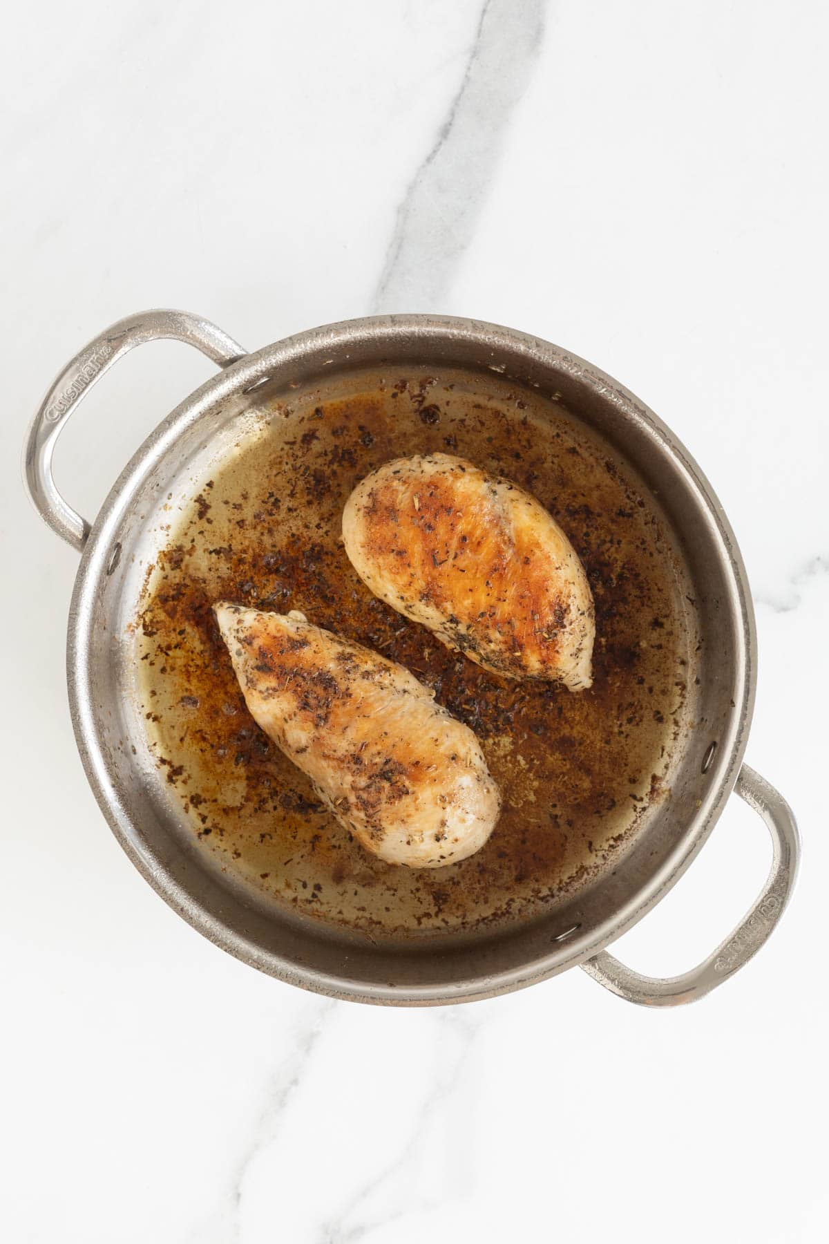 Two seasoned chicken breasts browned in a stainless steel pot
