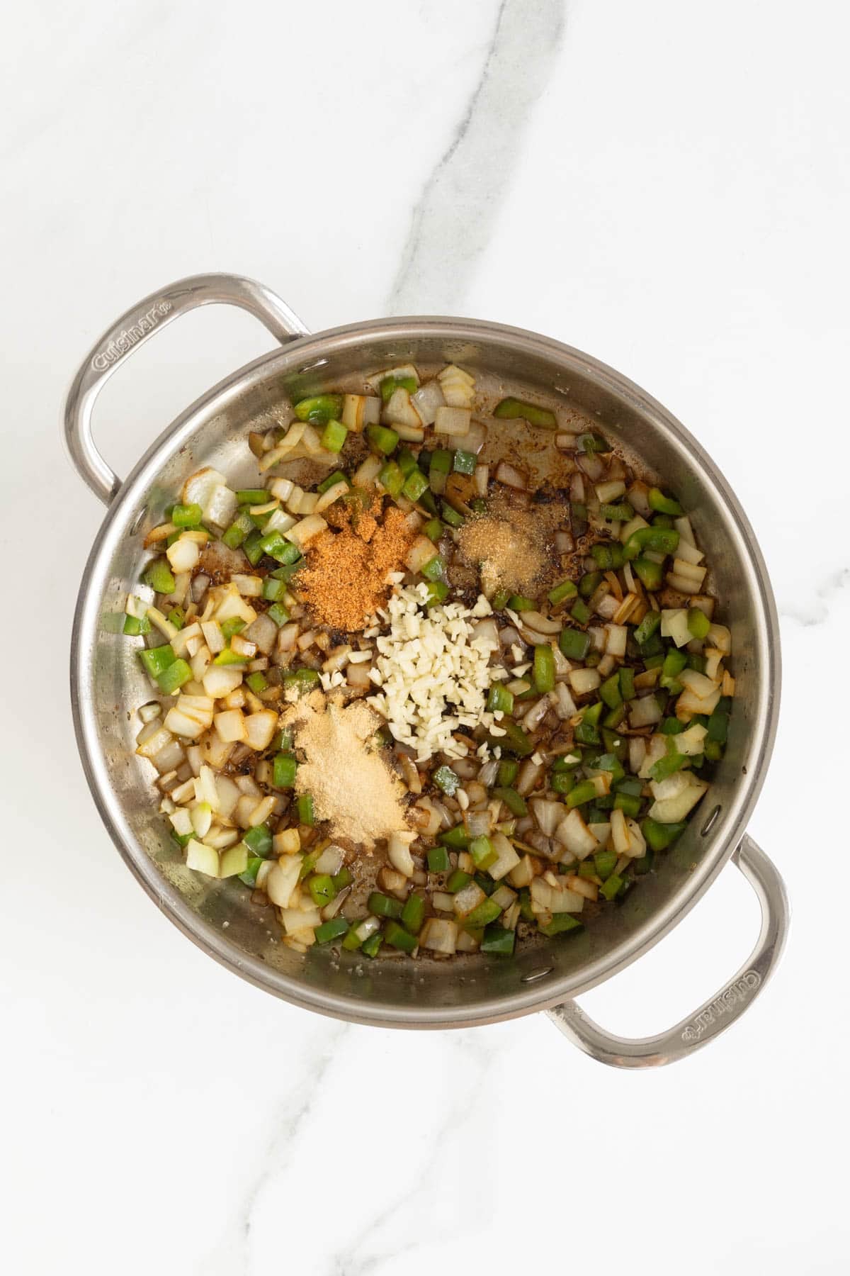 Diced onions and green bell peppers sautéing with garlic and spices in a pot