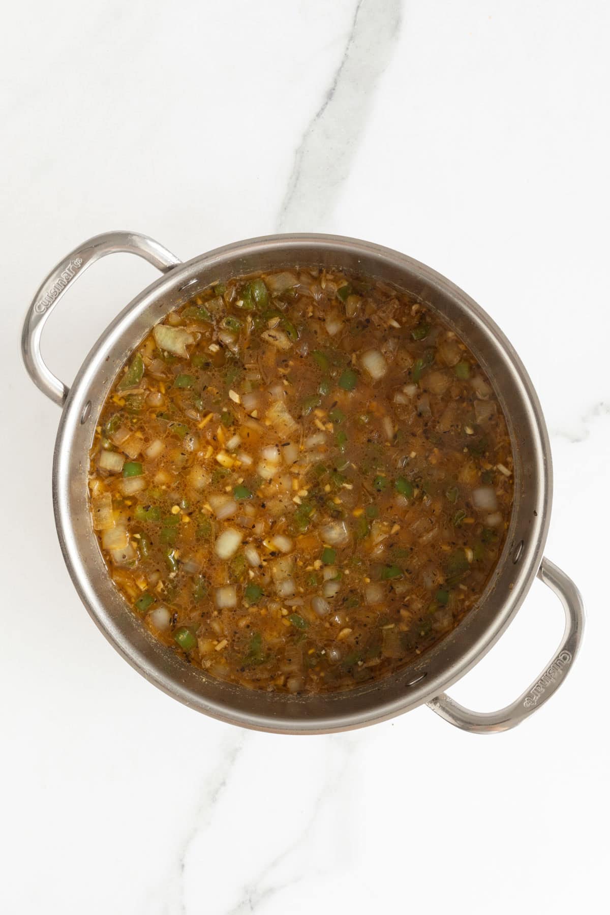 Cooked onions and peppers simmering in seasoned broth in a pot