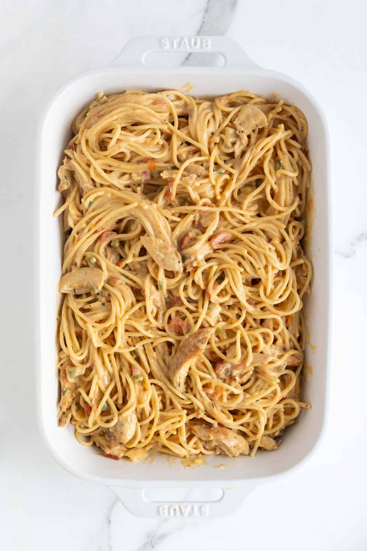 Cooked spaghetti and chicken mixed with creamy sauce in a baking dish