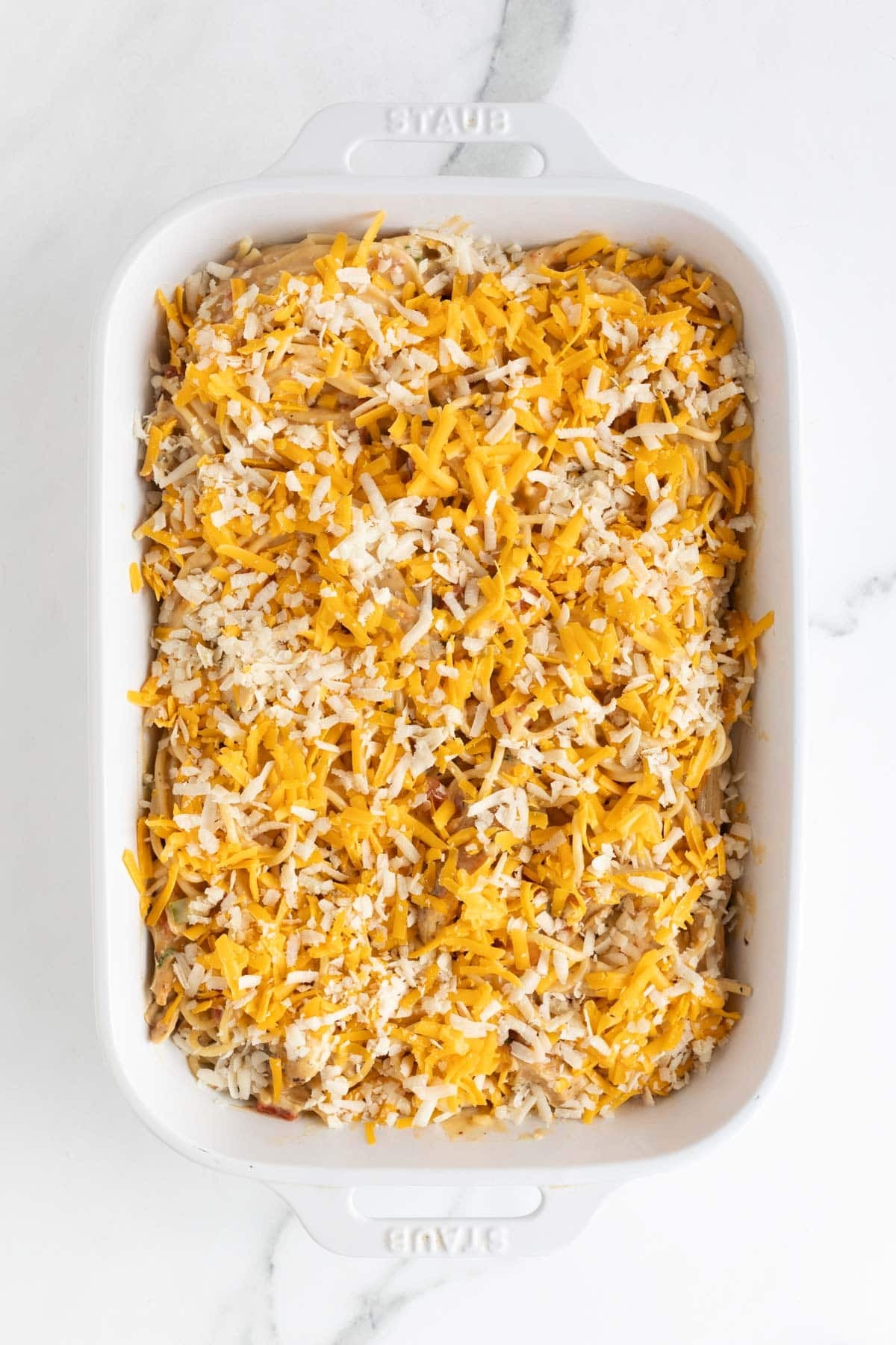Shredded cheese sprinkled over chicken spaghetti in a baking dish before baking