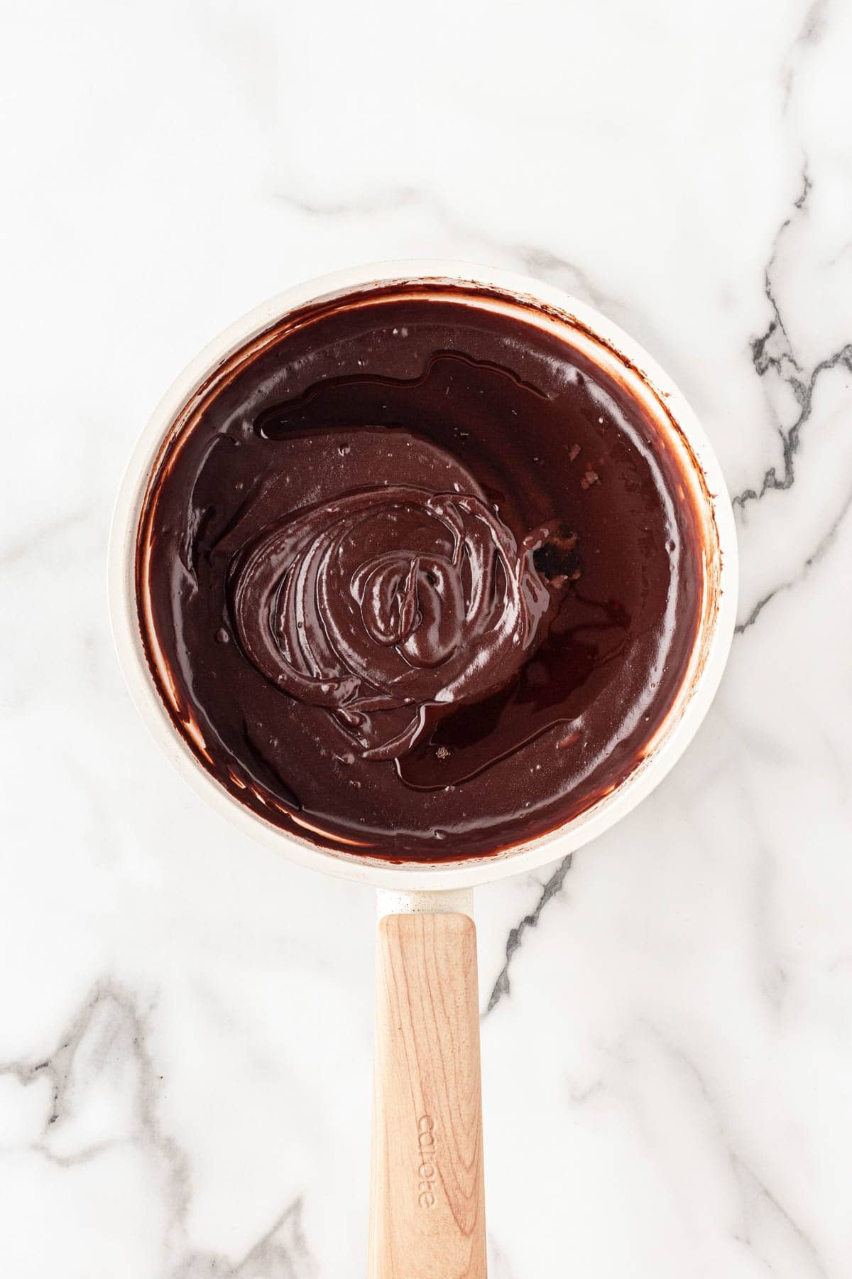 Glossy chocolate mixture stirred smooth inside a saucepan