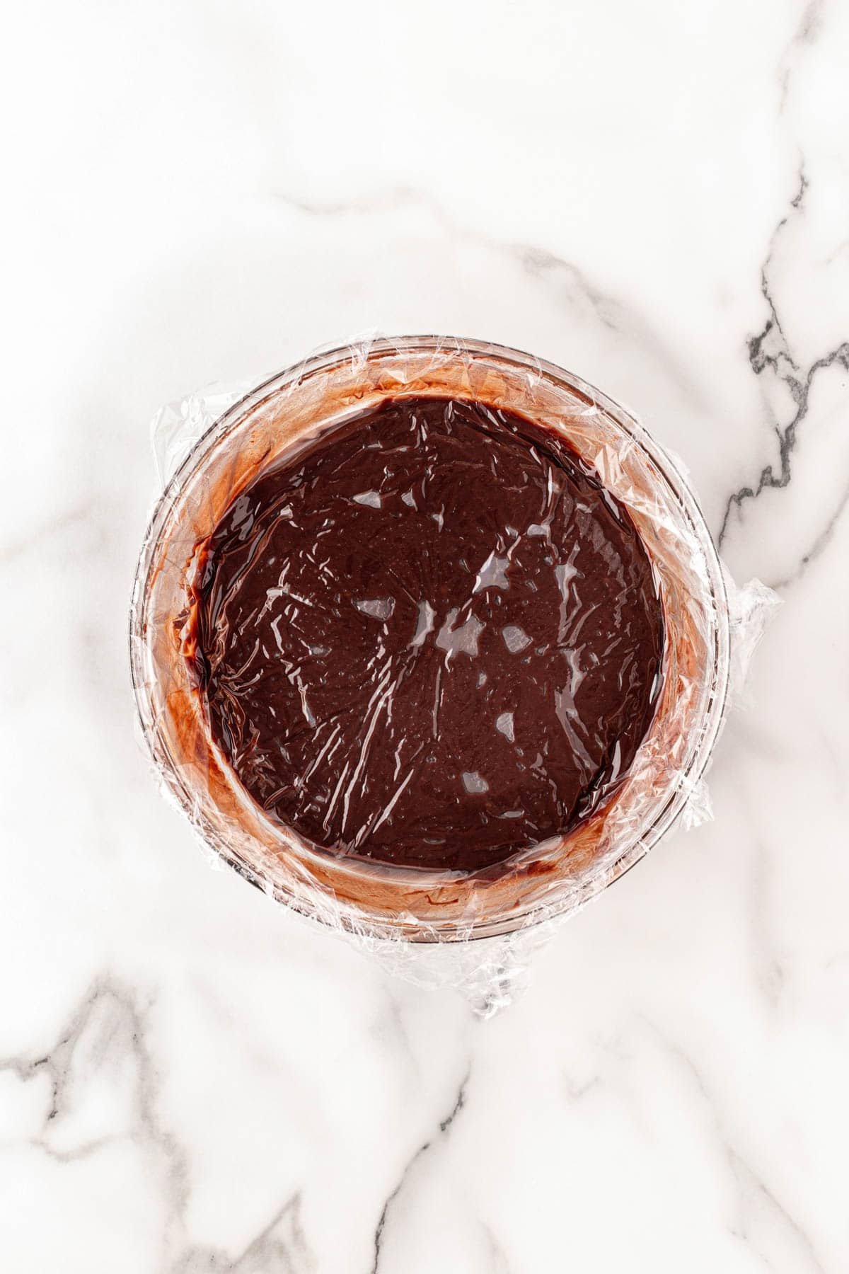 Chocolate mixture covered with plastic wrap to cool in a bowl