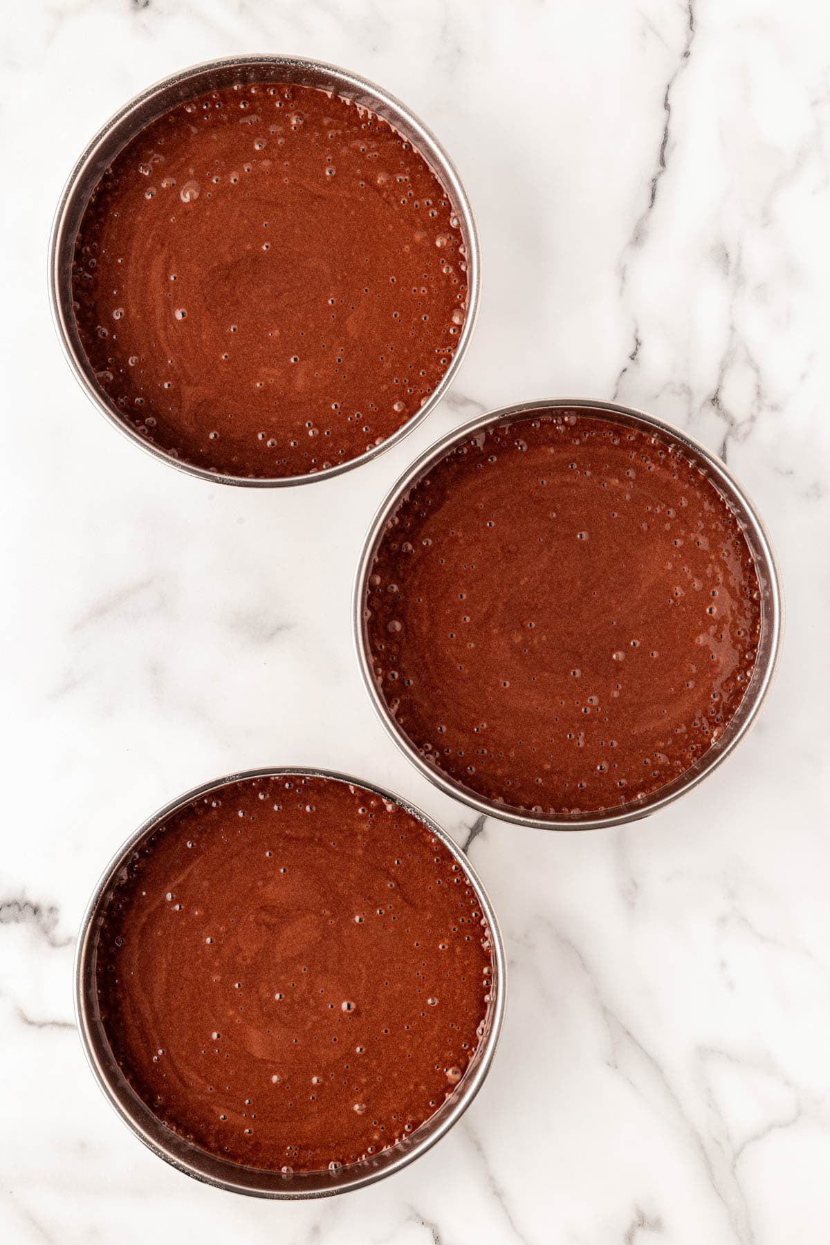 Three round cake pans filled with chocolate batter