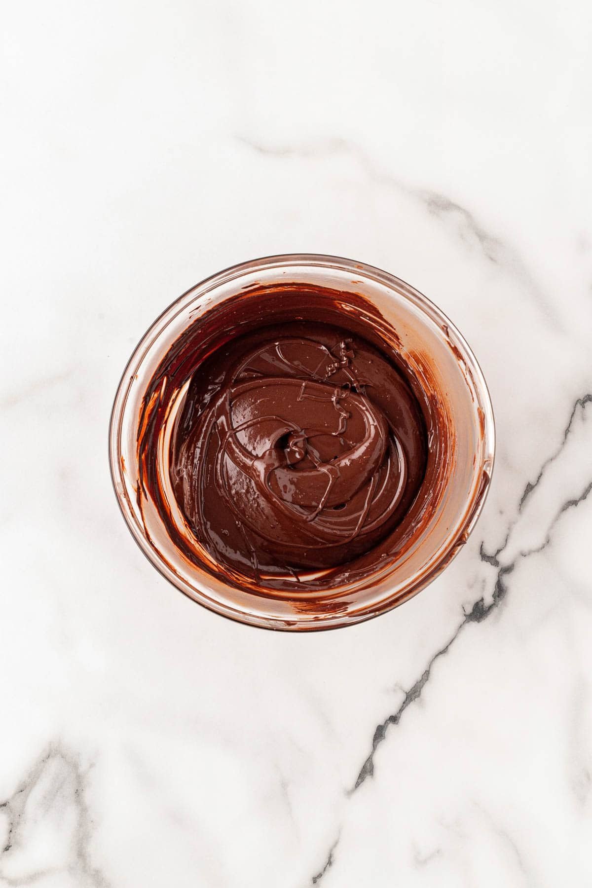 Melted chocolate mixture swirled in a glass bowl on a marble surface