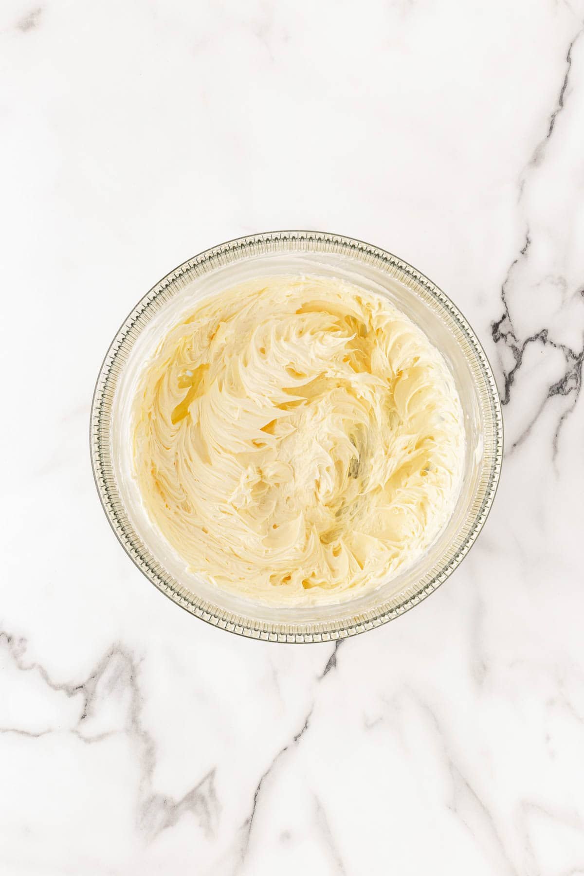 Whipped vanilla buttercream in a glass mixing bowl on a marble surface