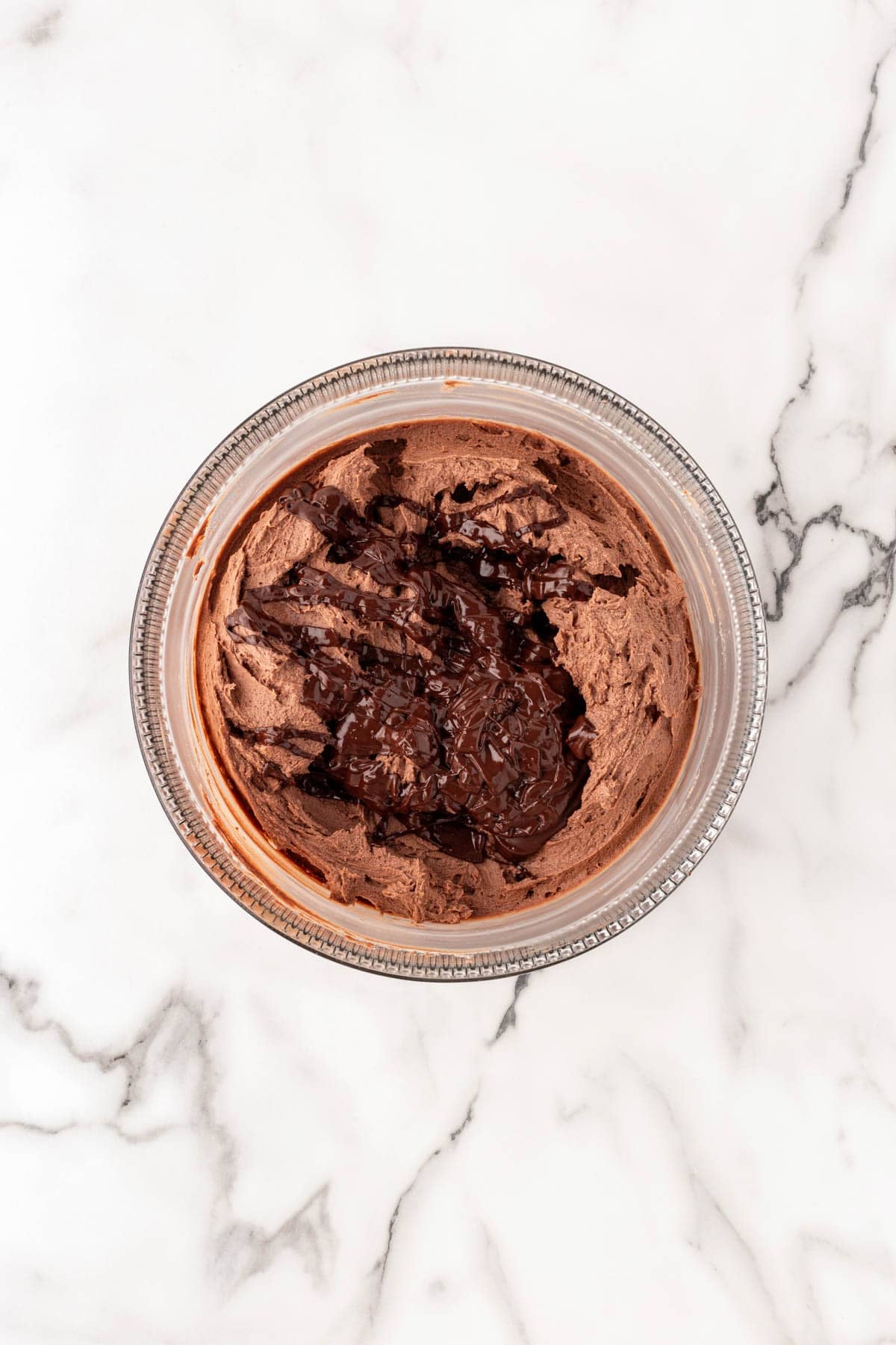 Chocolate buttercream in a mixing bowl with melted chocolate drizzled over the top