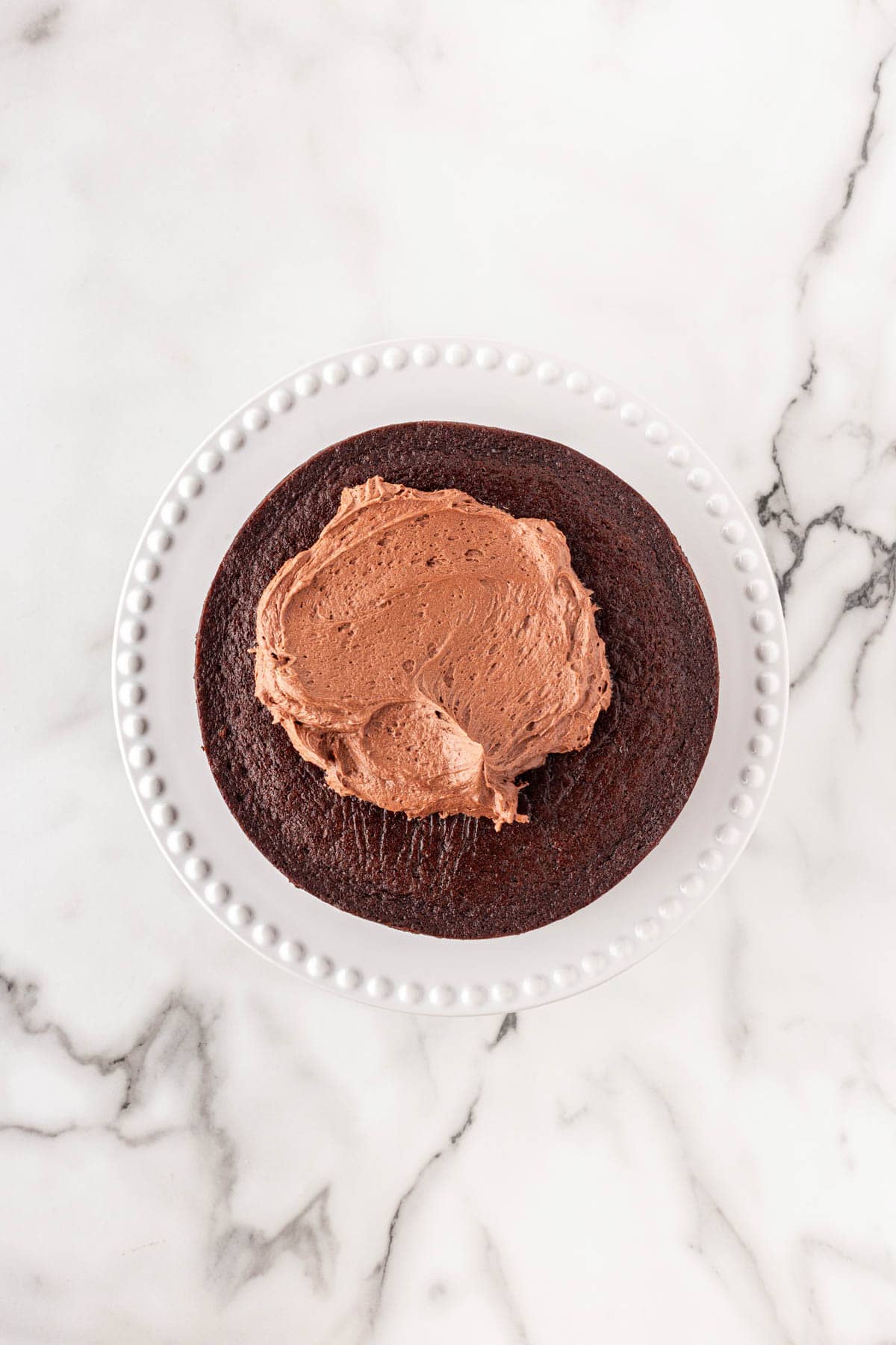 Chocolate cake layer on a cake stand with a dollop of chocolate buttercream spread in the center