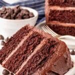 Two slices of chocolate cake with chocolate buttercream on a plate beside chocolate chips
