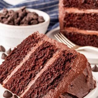 Two slices of chocolate cake with chocolate buttercream on a plate beside chocolate chips