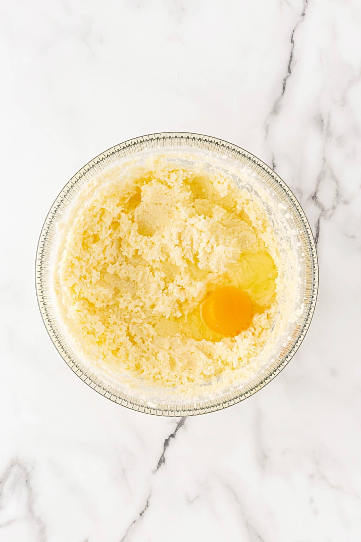 Creamed butter and sugar mixture in a glass bowl with a whole egg added on top